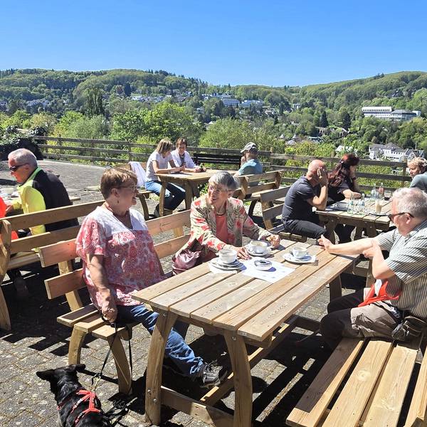 Menschen sitzen auf einer Café-Terrasse in der Sonne und genießen Kaffee, Kuchen und den Ausblick auf Bad Münstereifel.