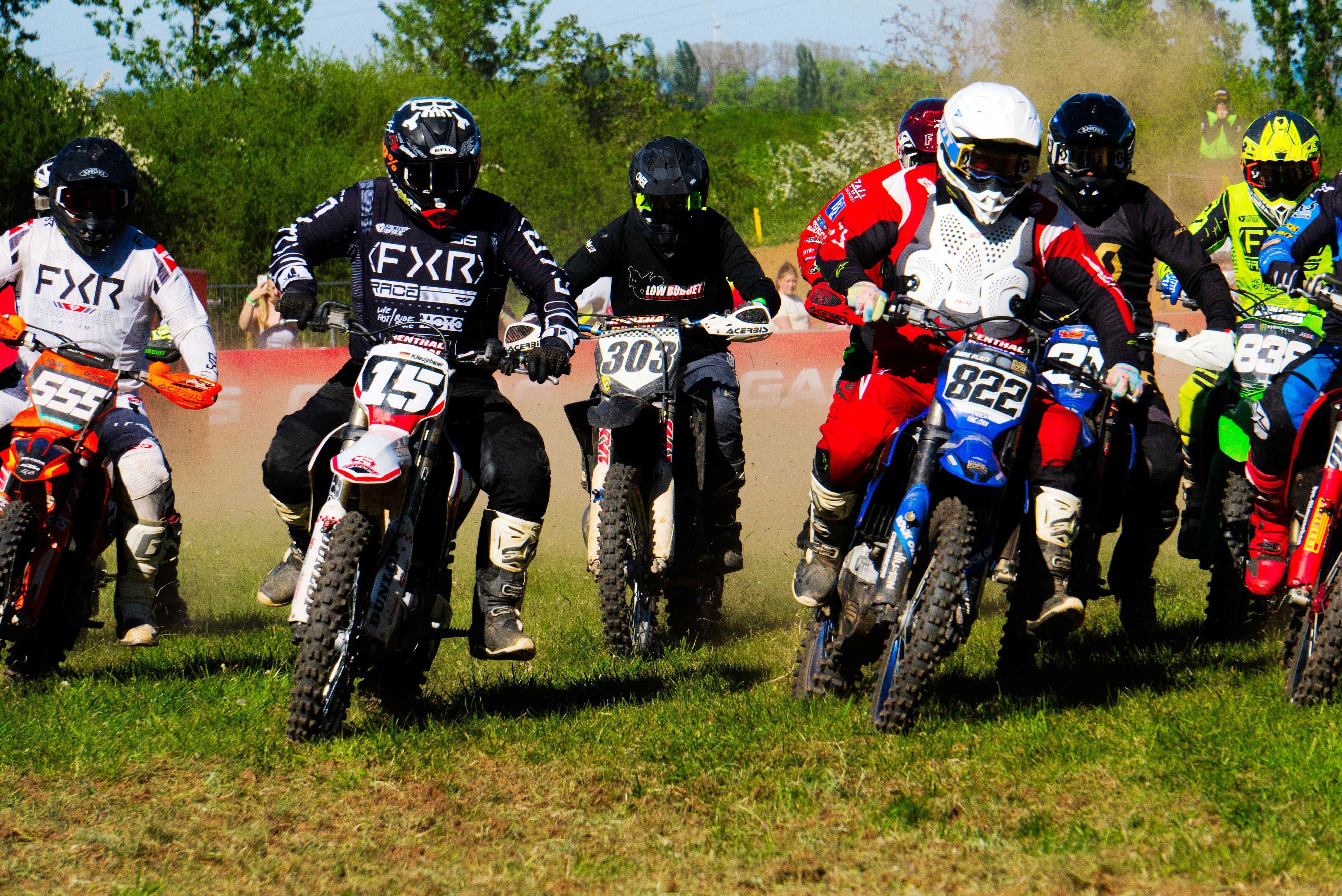 Zahlreiche Motocross-Maschinen fahren beinahe nebeneinander über die Strecke.