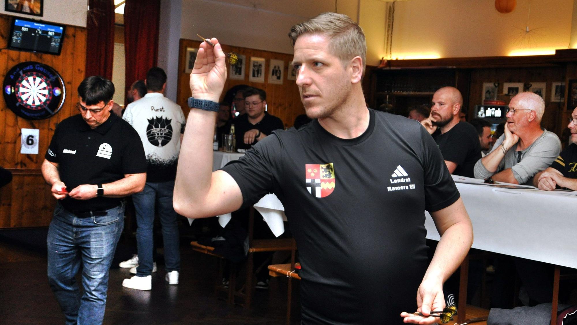 Landrat Markus Ramers im schwarzen T-Shirt mit Kreis-Wappen beim Dartturnier in Kall.