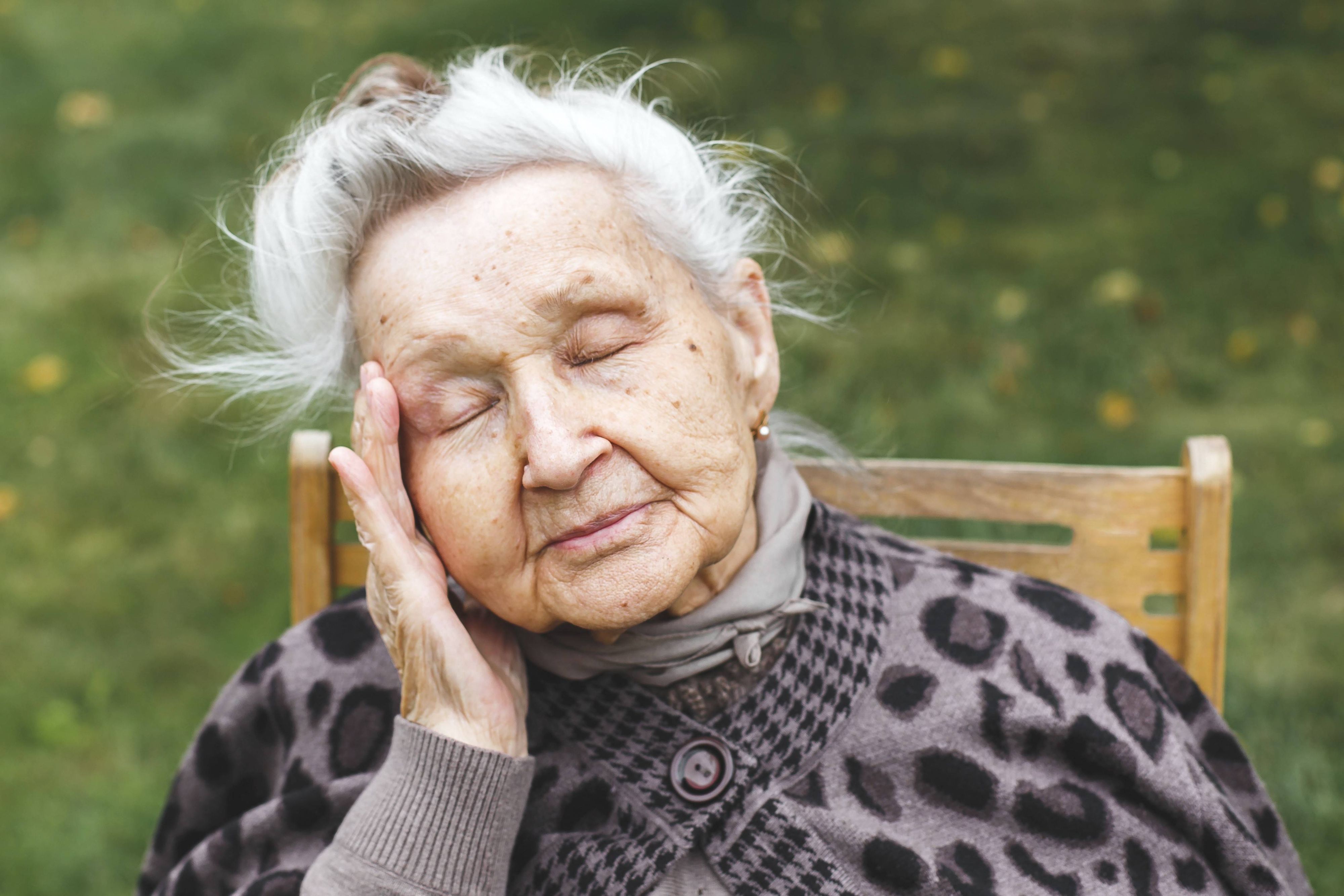 Ältere Frau mit geschlossenen Augen, die ihren Kopf berührt, Müdigkeit oder Unwohlsein ausdrückt.