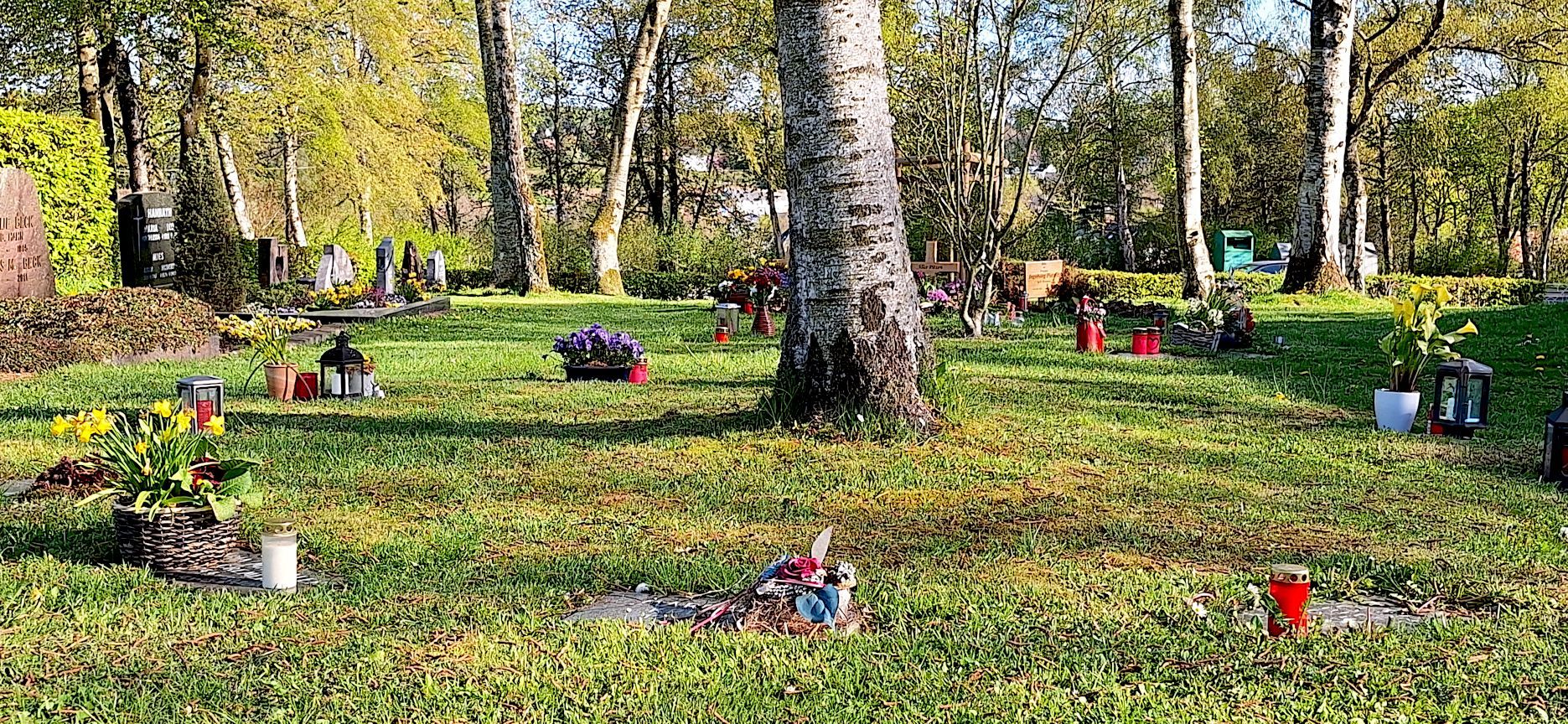 Auf den Grabplatten der Rasengräber in Schmidtheim sind Blumenschmuck, Grablichter und Figürchen zu sehen.