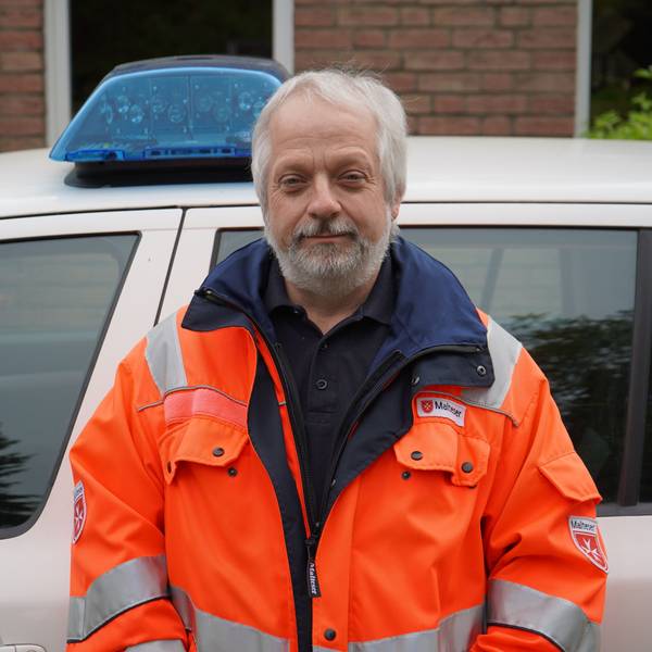 Das Bild zeigt Hornfeck mit einer orangen Jacke vor einem Dienstwagen mit Blaulicht.