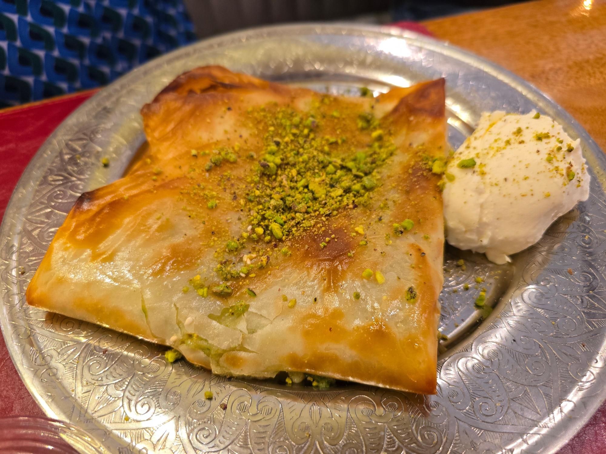 Ein gefalteter Teig mit Pistazienbröseln und Eis daneben auf silbernem Teller