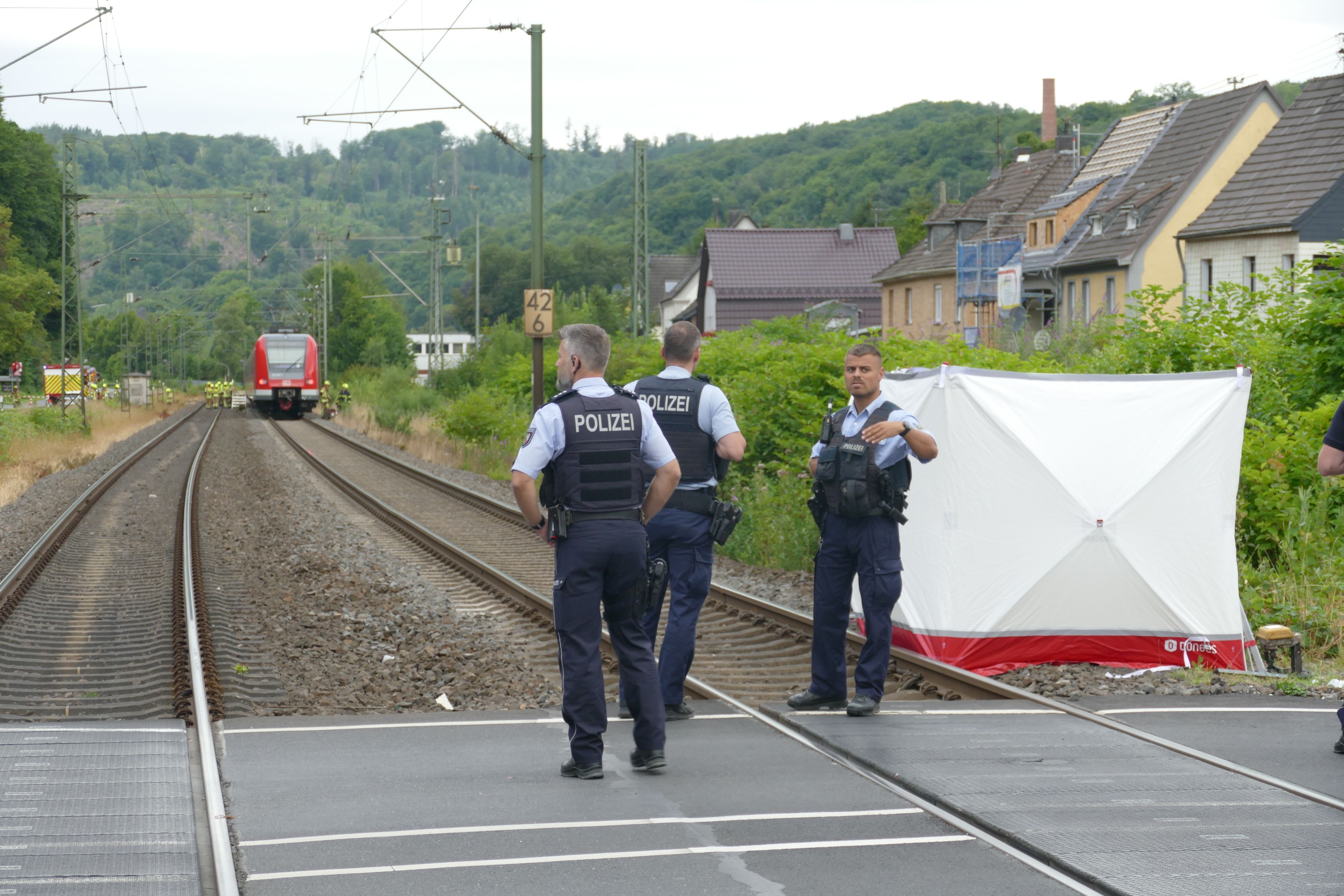 Polizisten stehen nach einem Unfall mit einem Zug an einem Bahnübergang.