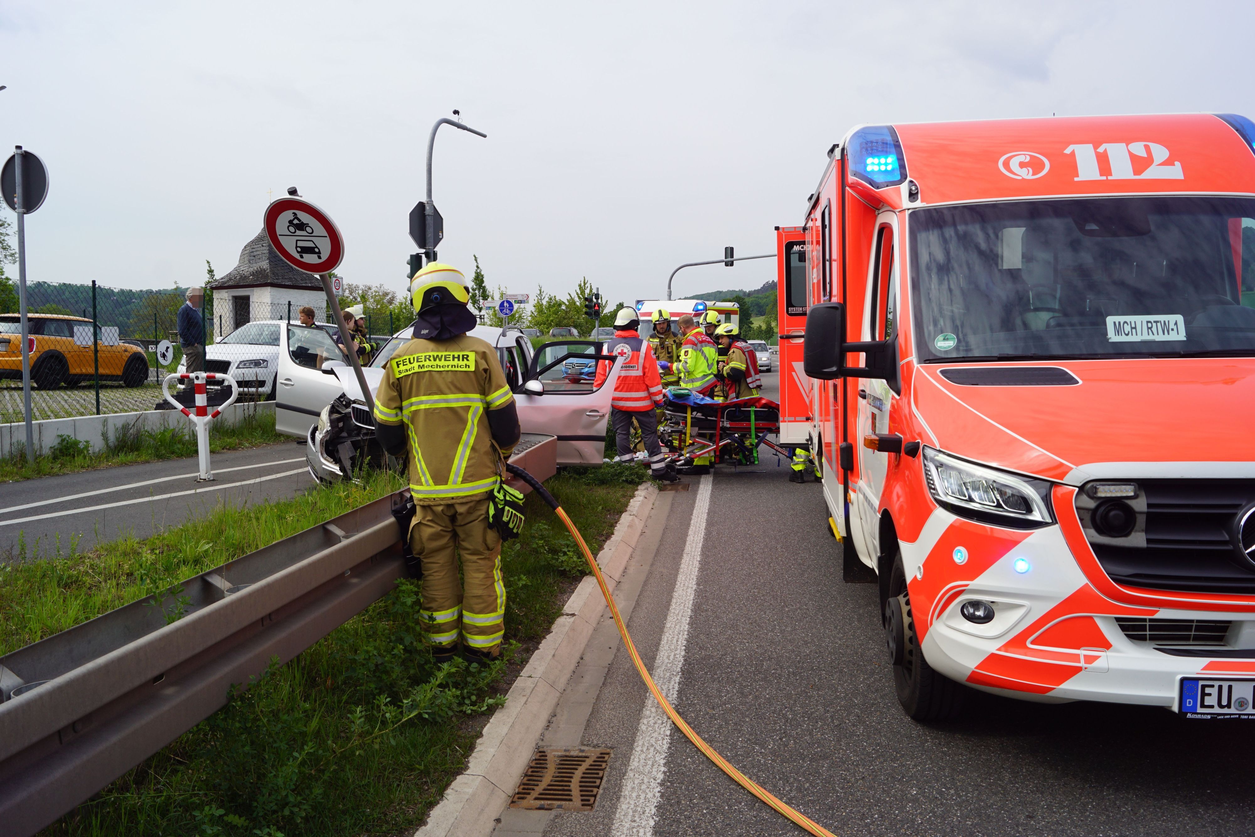 Rechts ist ein Rettungswagen zu sehen, daneben stehen Einsatzkräfte an einem verunfallten Auto.