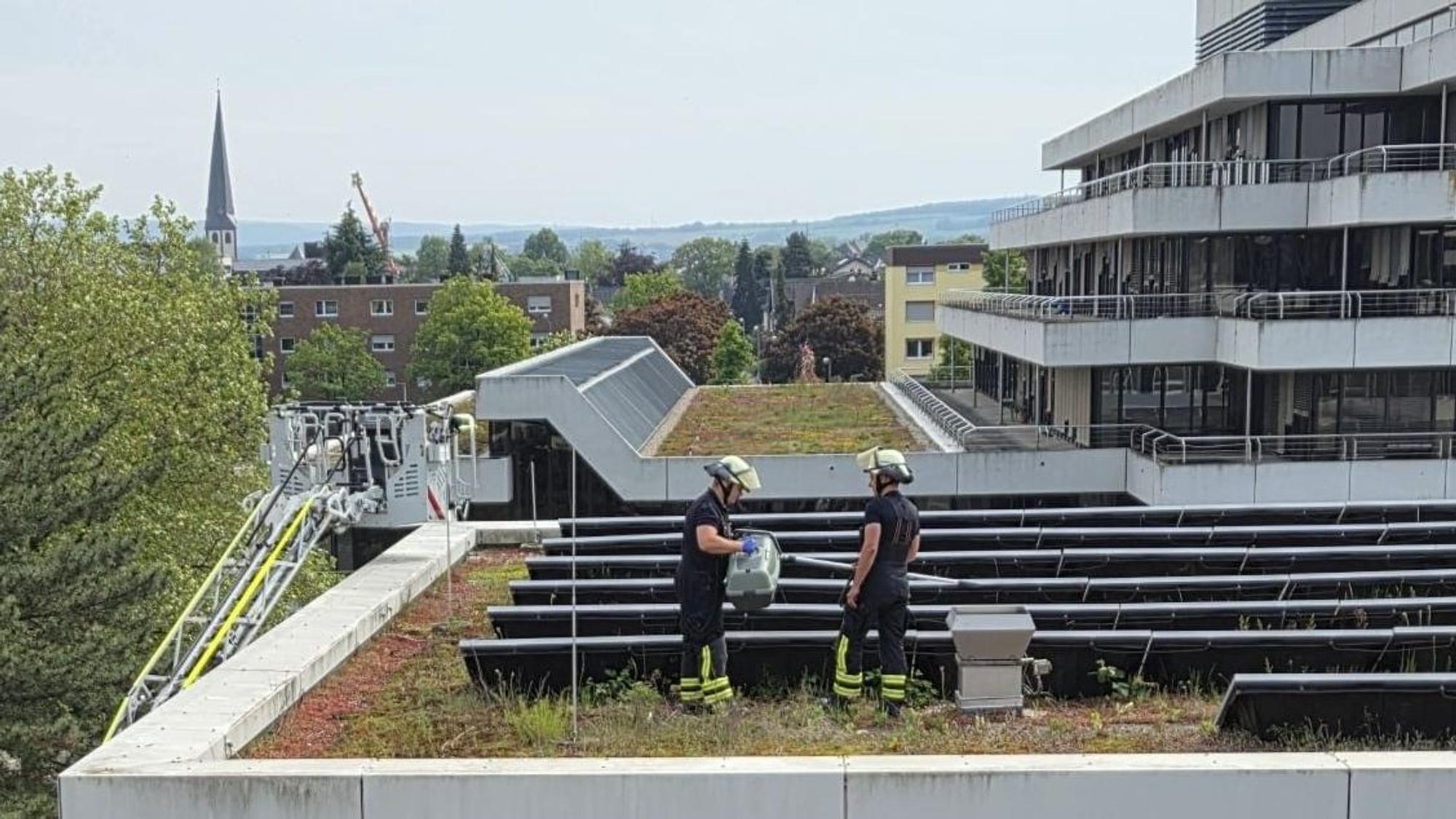 Zwei Feuerwehrleute stehen auf dem Dach des Kreishauses in Euskirchen. Links ist der Korb der Drehleiter zu sehen.