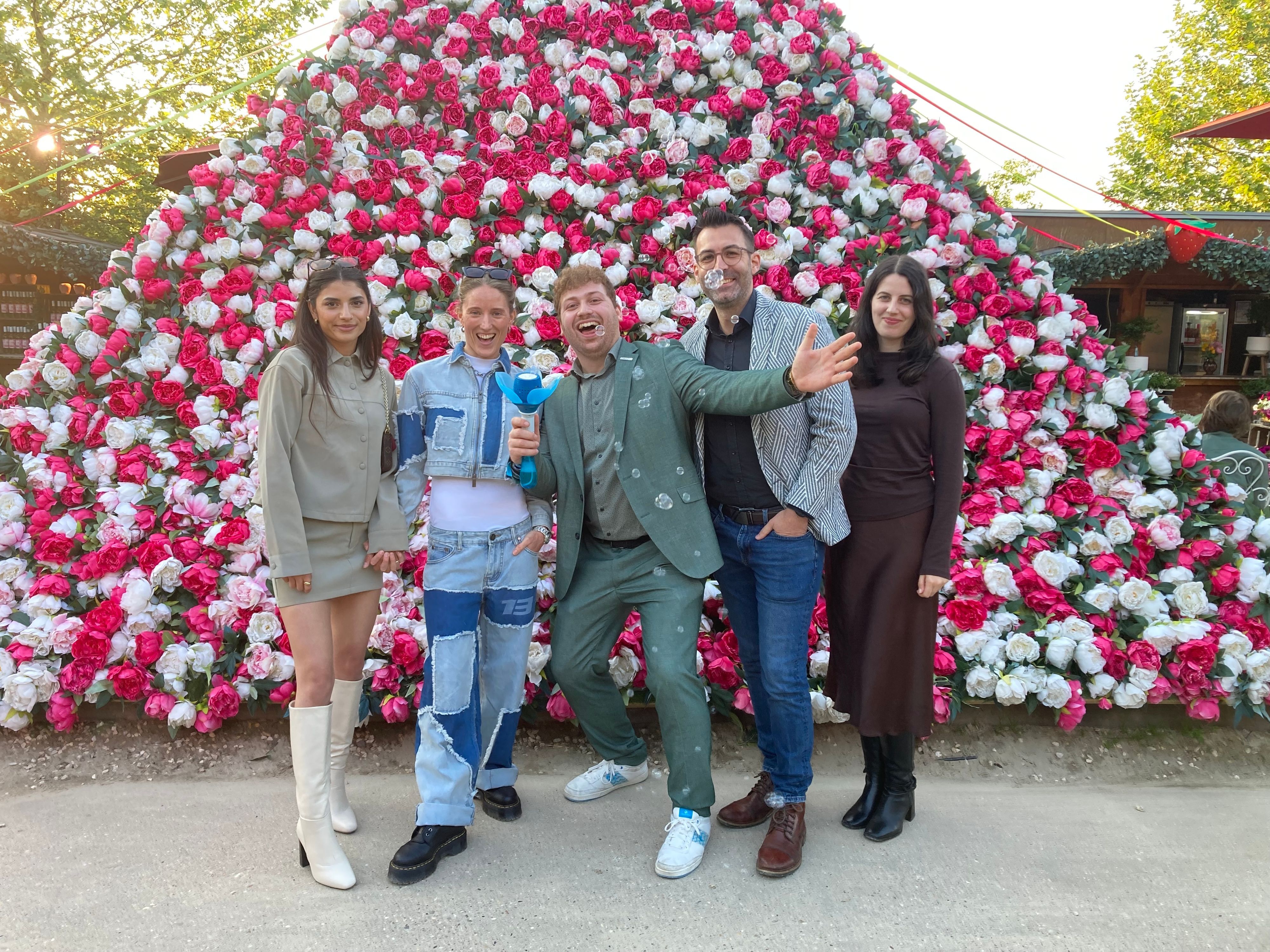 Auf dem Bild ist eine Gruppe von jungen Leuten zu sehen, die vor einer Pyramide aus Blumen stehen.
