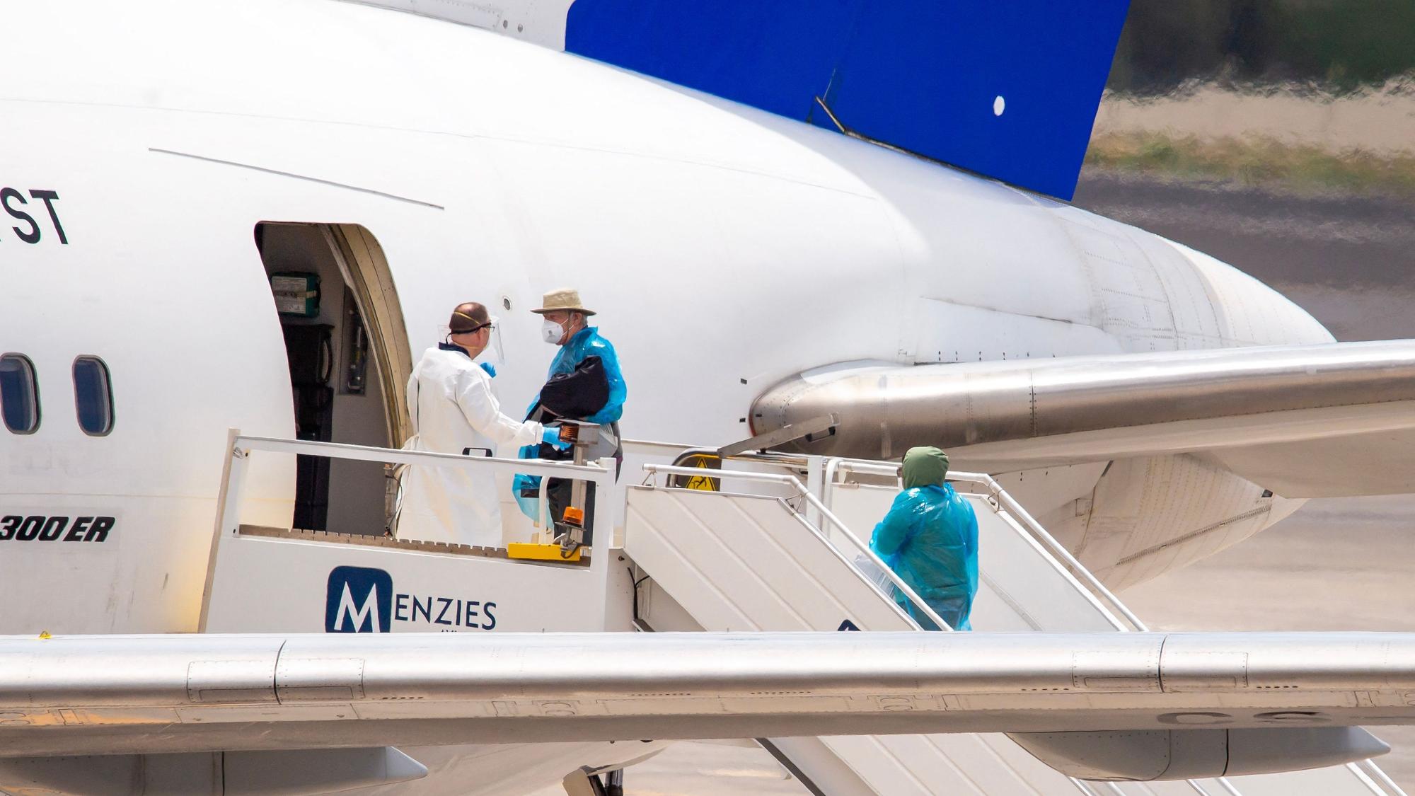 Passagiere in Schutzanzügen betreten ein Flugzeug.