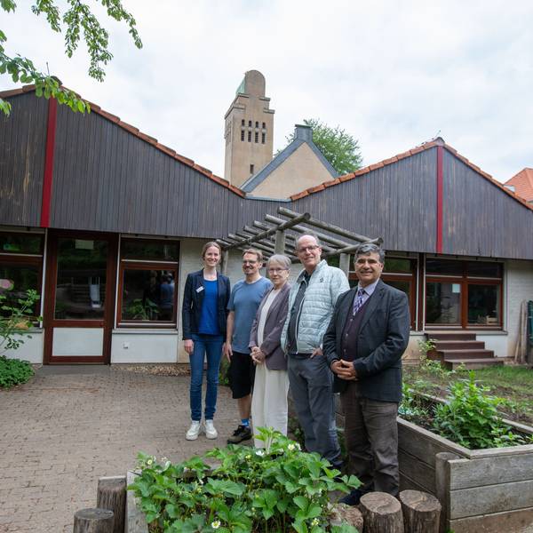 Drei Männer und zwei Frauen stehen im mit Hochbeeten gestalteten Bereich vor einer Kita.