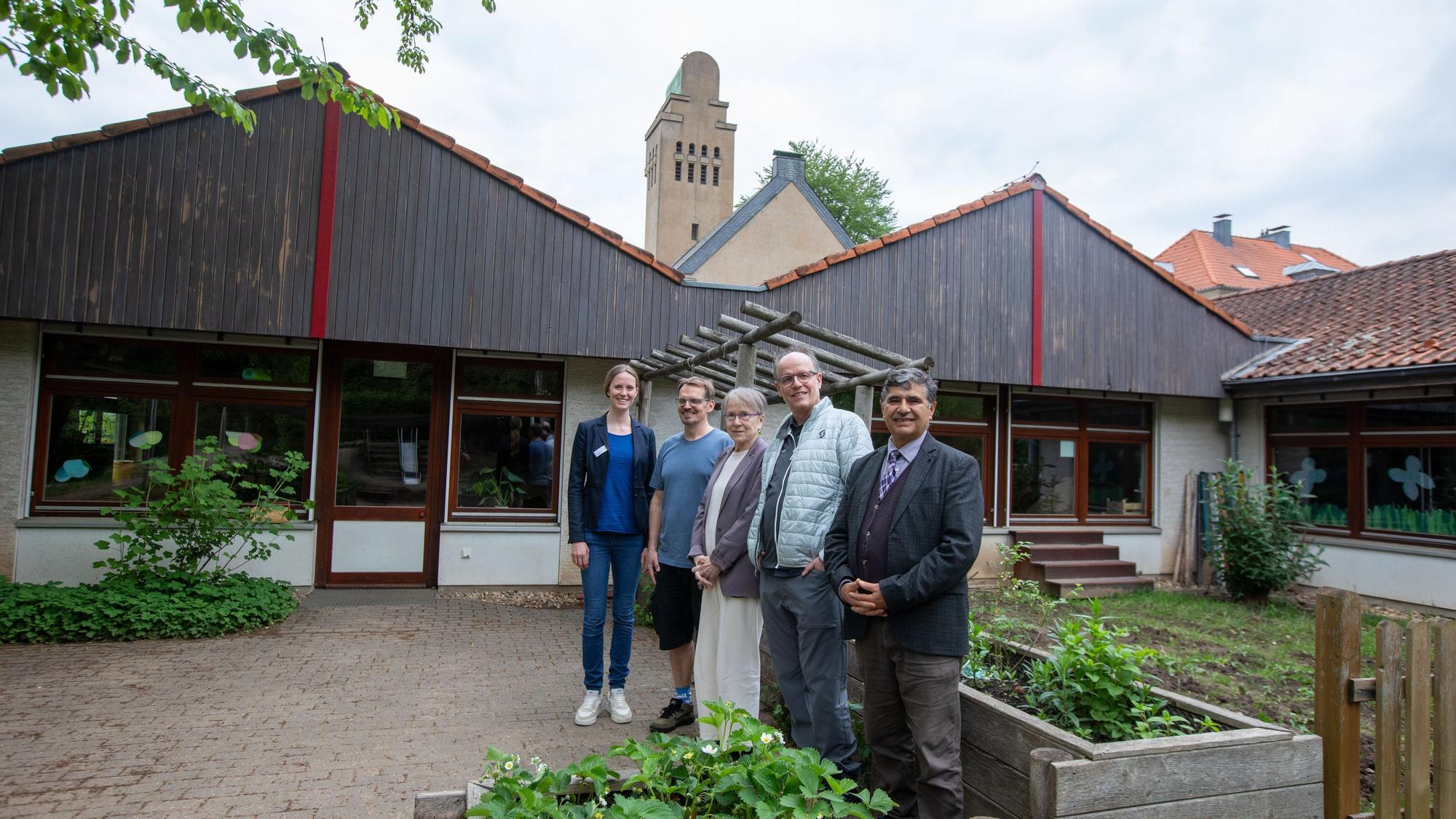 Drei Männer und zwei Frauen stehen im mit Hochbeeten gestalteten Bereich vor einer Kita.