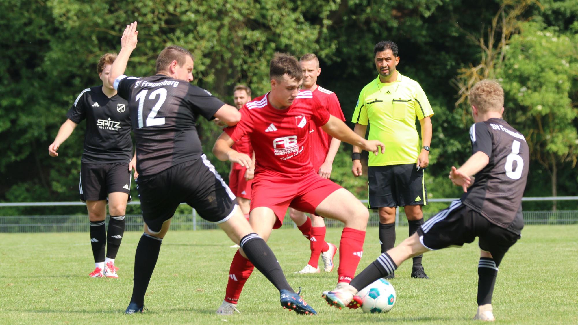Fußballer Tim Breuer vom TSV Schönau im roten Trikot setzt sich gegen zwei Spieler des SV Frauenberg in schwarzen Trikots durch.