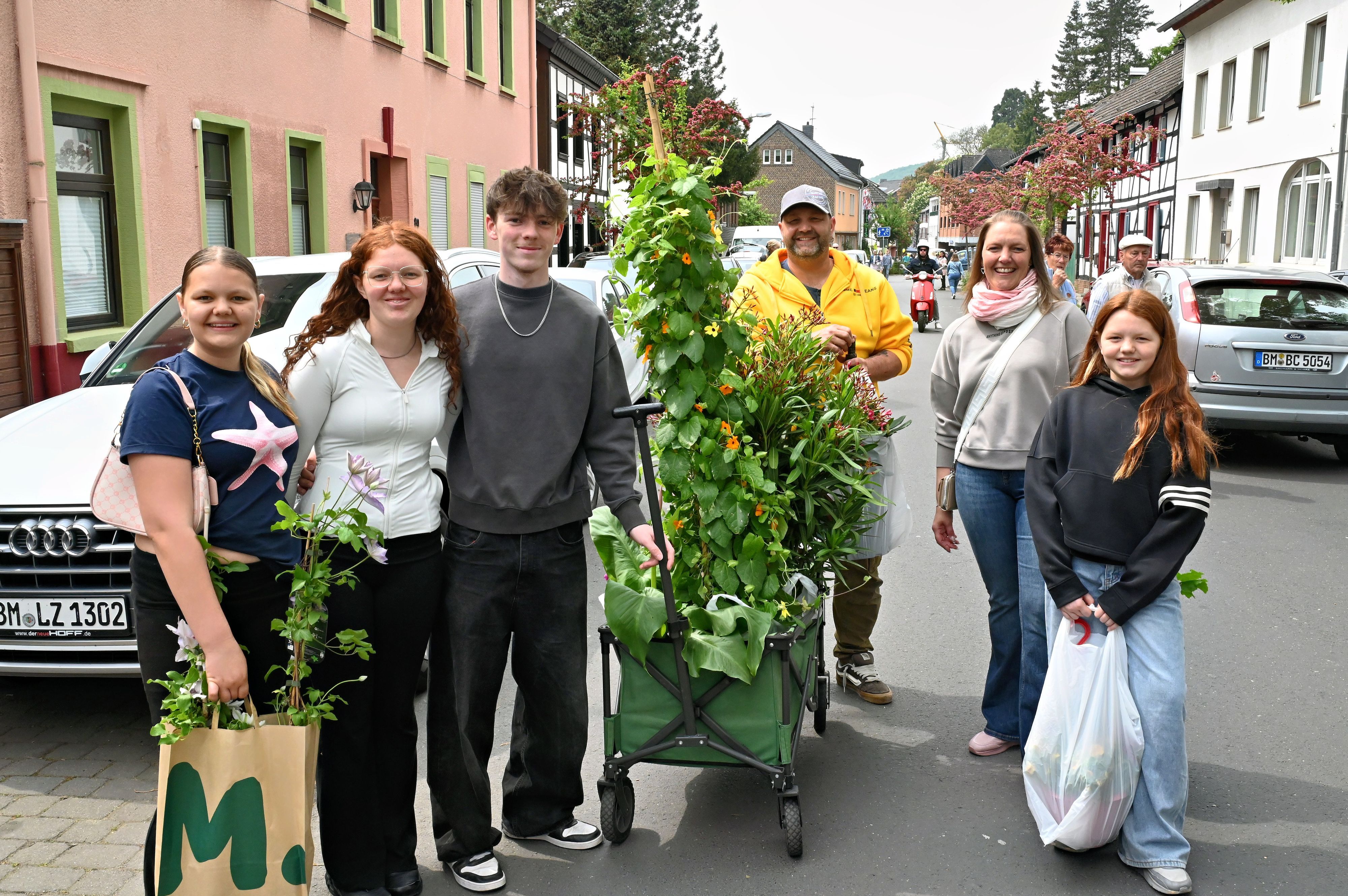 Sechs Menschen haben sich um einen Bollerwagen mit großen Pflanzen aufgestellt.