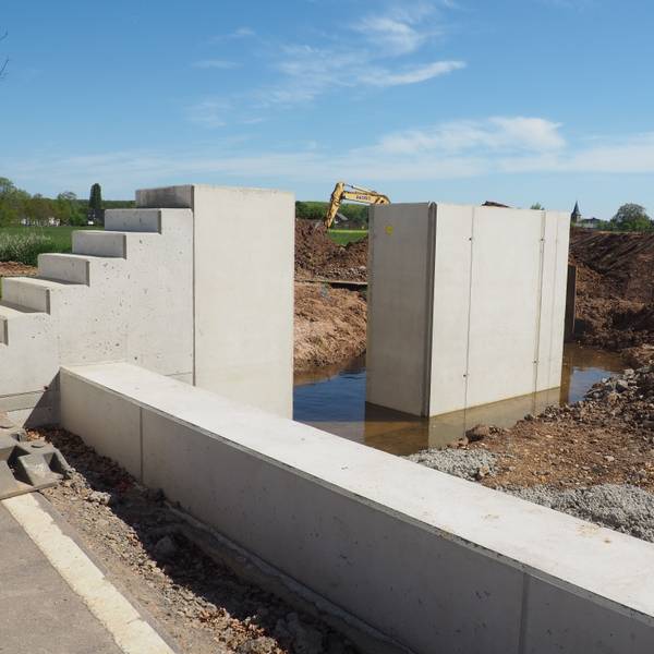 Im Vordergrund verläuft die Schwelle, hinter der später der Vlattener Bach fließen wird. Eine Betontreppe führt aufwärts bis zu einer Lücke zwischen zwei Betonelementen.