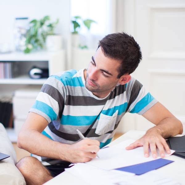Ein Mann sitzt vor einem Laptop, der auf einem Sofa steht, und schreibt auf einem Papier.
