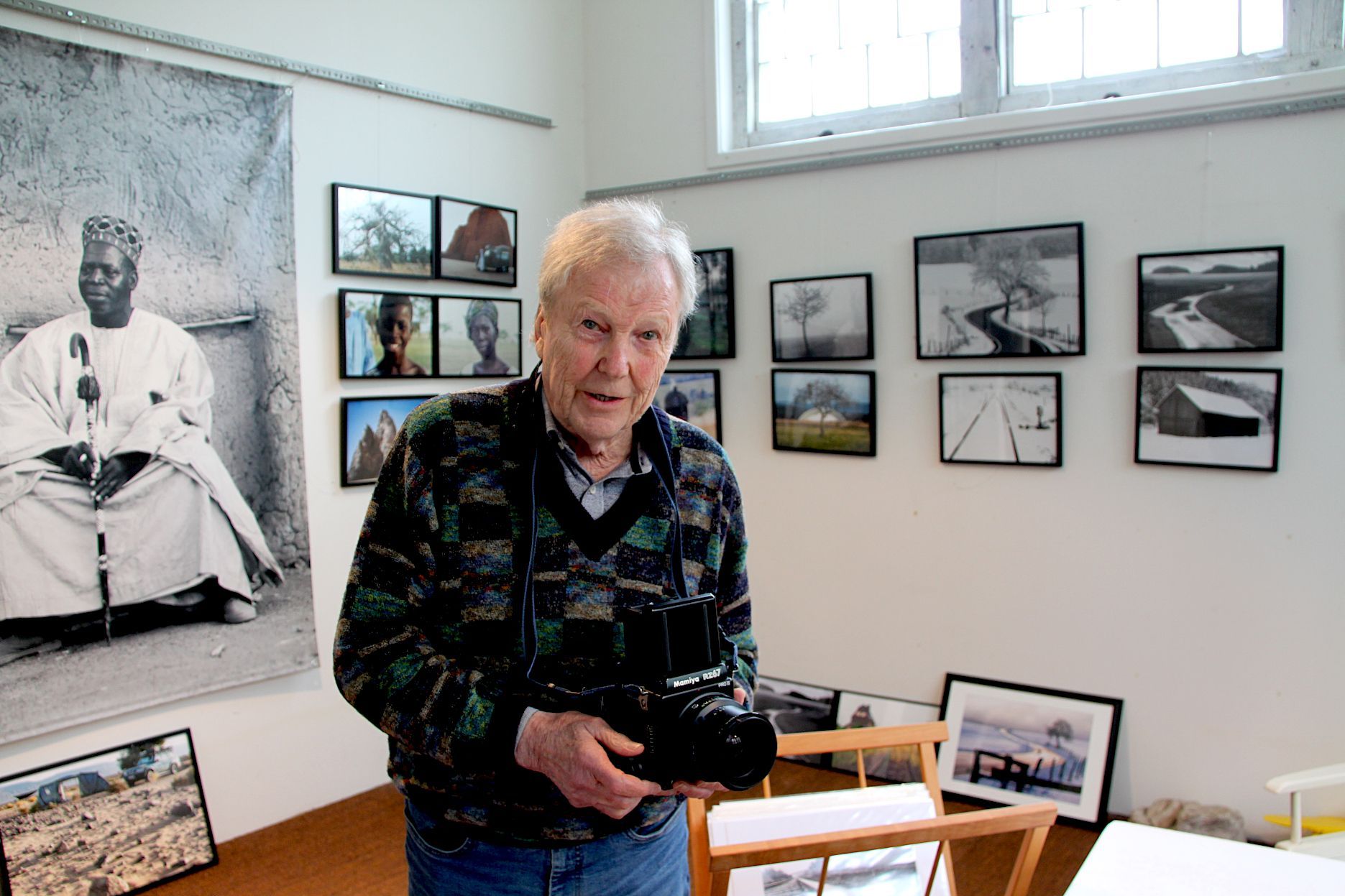 Dietrich Schubert mit einer Kamera, umringt von seinen Fotografien.