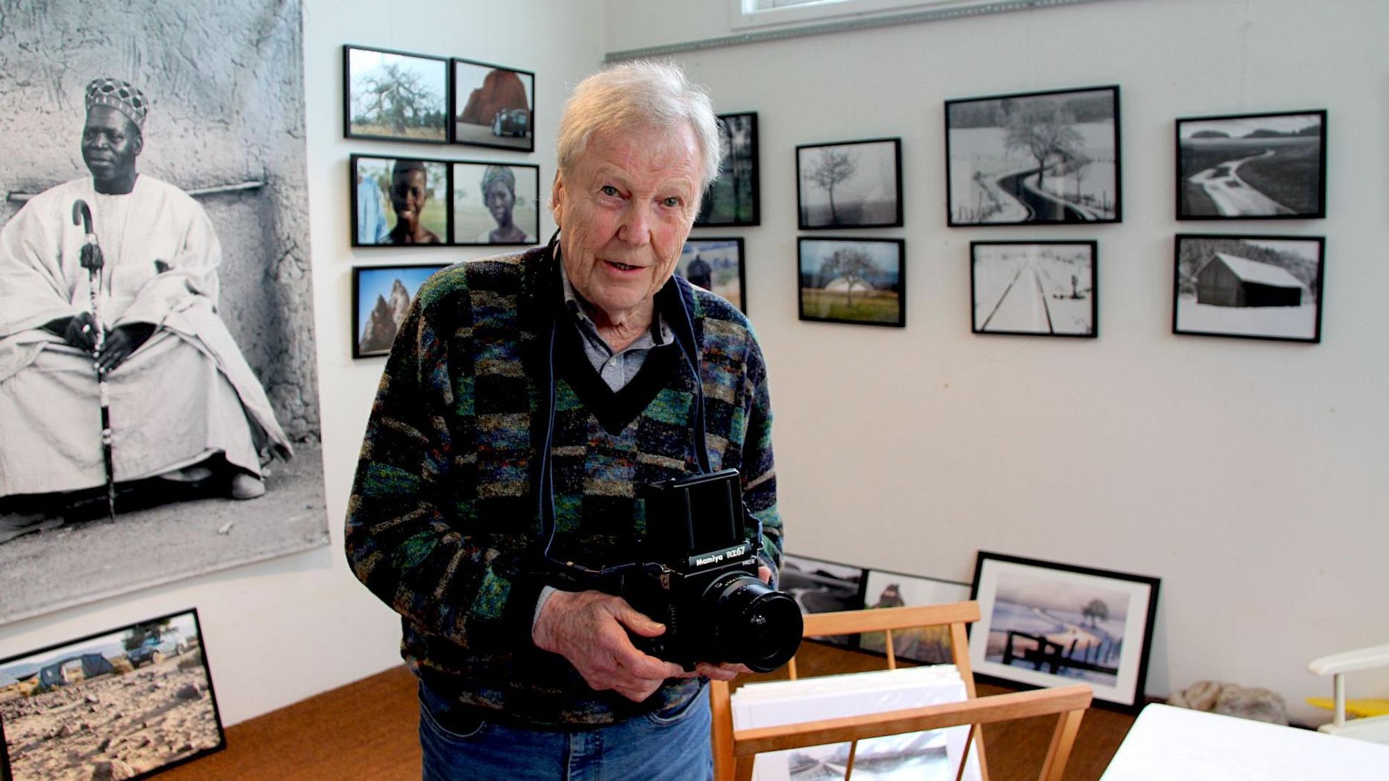 Dietrich Schubert mit einer Kamera, umringt von seinen Fotografien.