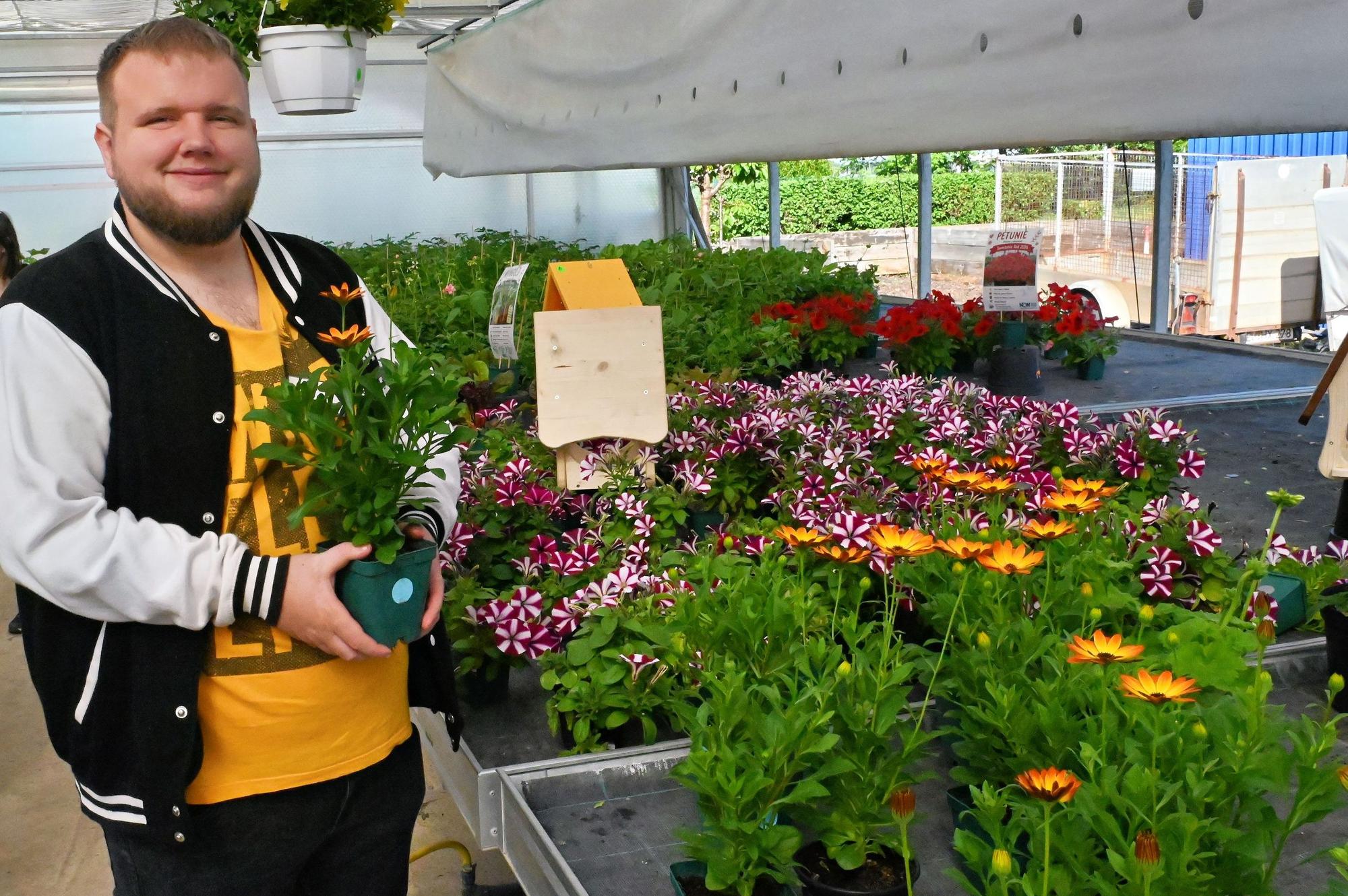 Sebastian Tholl hält eine Blume in der Hand, neben ihm stehen weitere blühende Pflanzen.