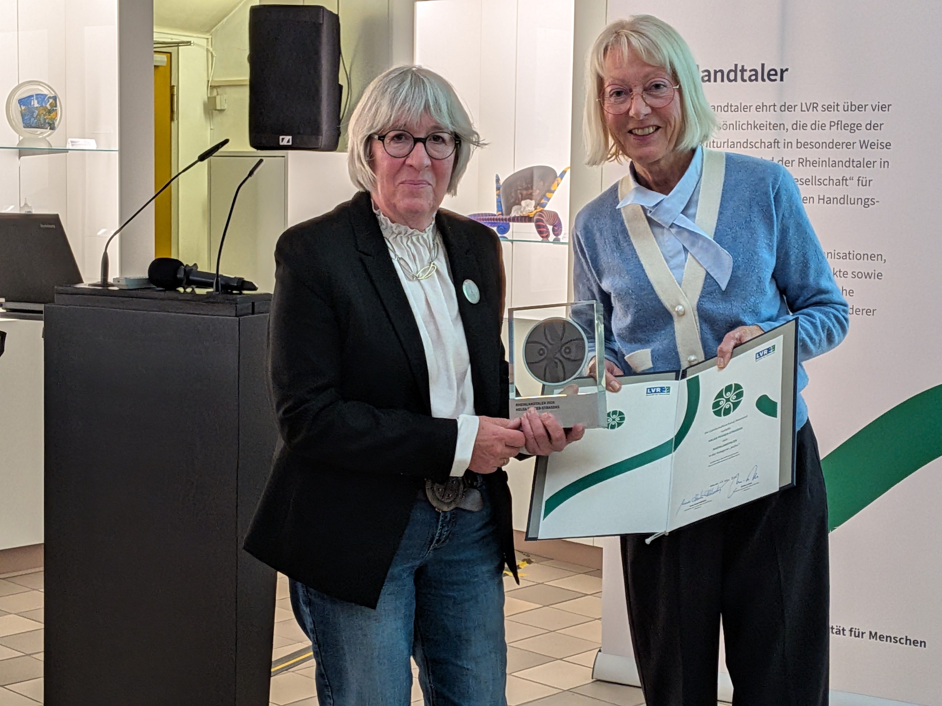 Elfi Scho-Antwerpes (rechts) überreicht den Rheinlandtaler mit Urkunde an Helga Feuser-Strasdas (links).