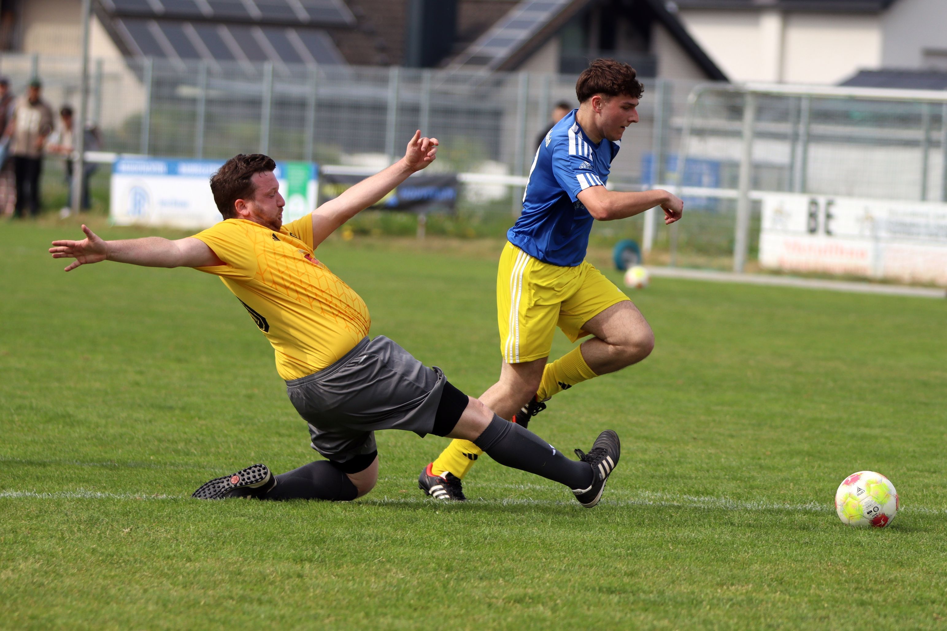 Ein Fußballer legt den Ball an einem grätschenden Verteidiger vorbei.