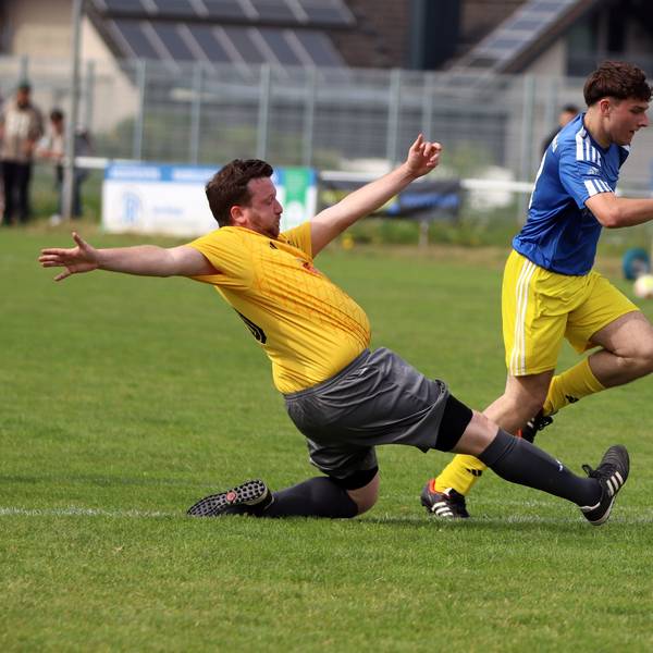 Ein Fußballer legt den Ball an einem grätschenden Verteidiger vorbei.