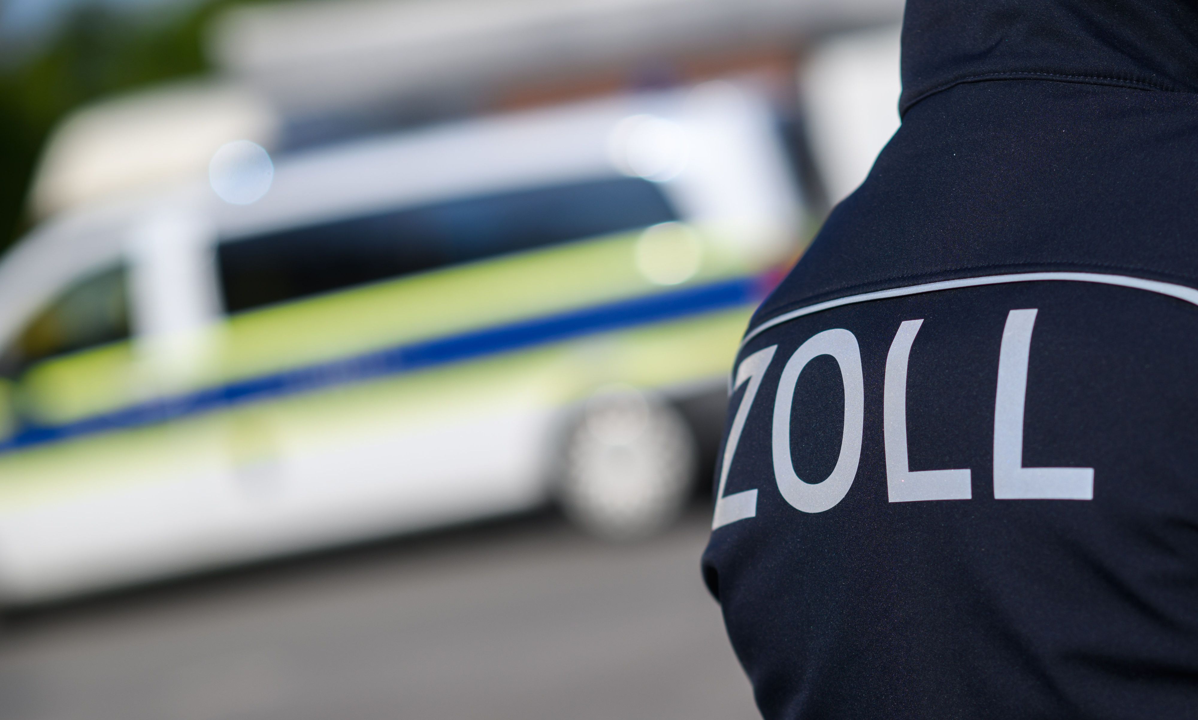 Zollbeamte stehen bei einer Kontrolle neben Einsatzwagen.