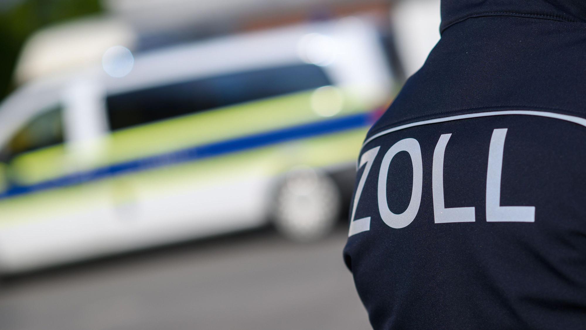 Zollbeamte stehen bei einer Kontrolle neben Einsatzwagen.
