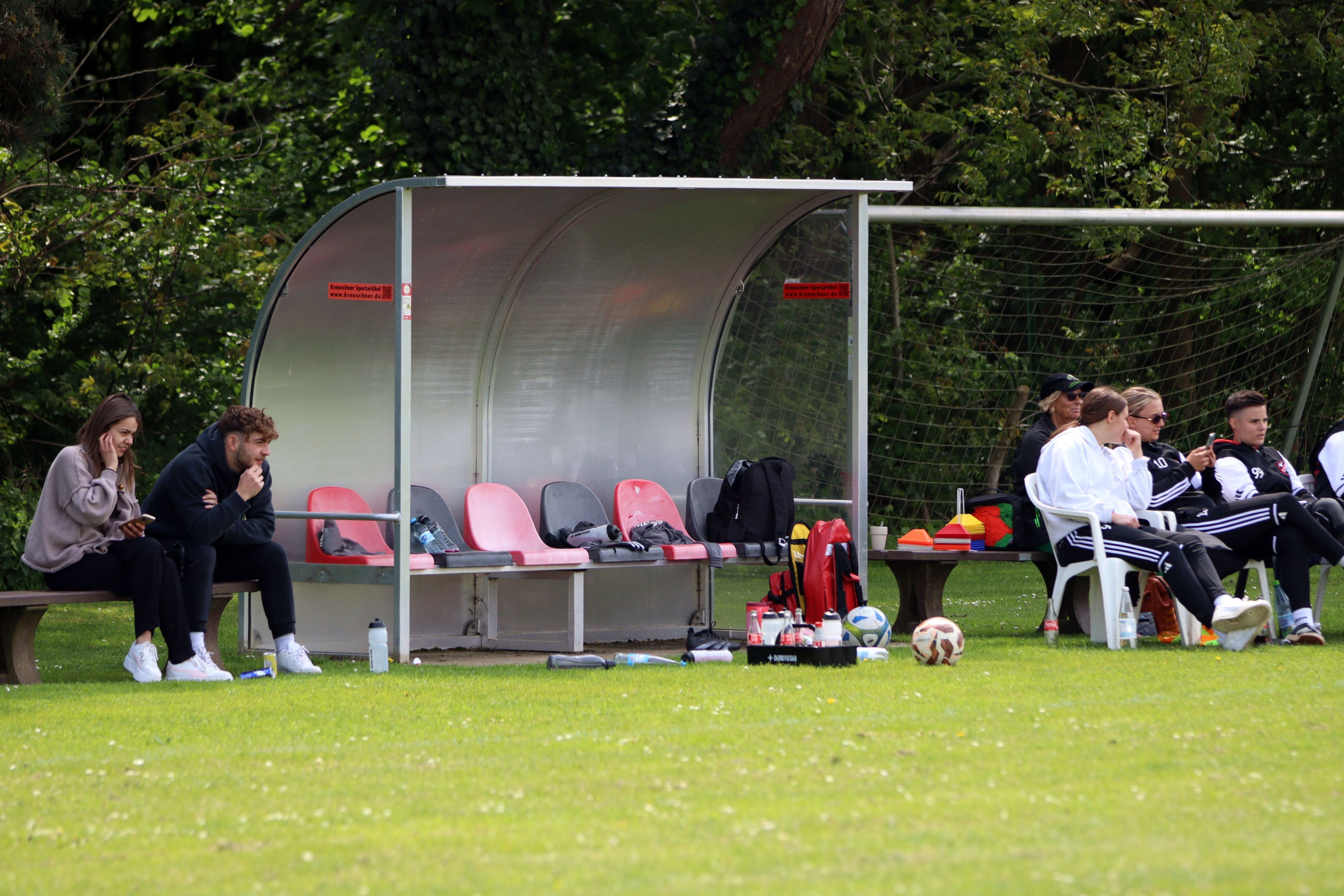 Die leere Ersatzbank der Heimmannschaft. Daneben sitzen Zuschauer, darunter auch verletzte Spielerinnen, auf Stühlen.