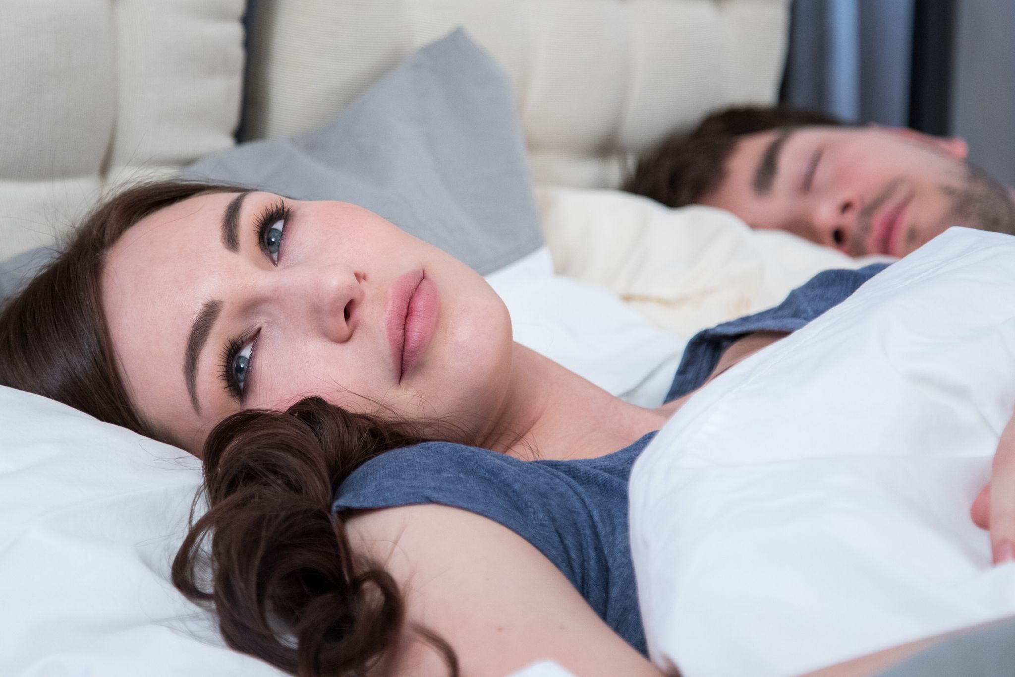 Eine junge Frau liegt wach neben ihrem Partner im Bett