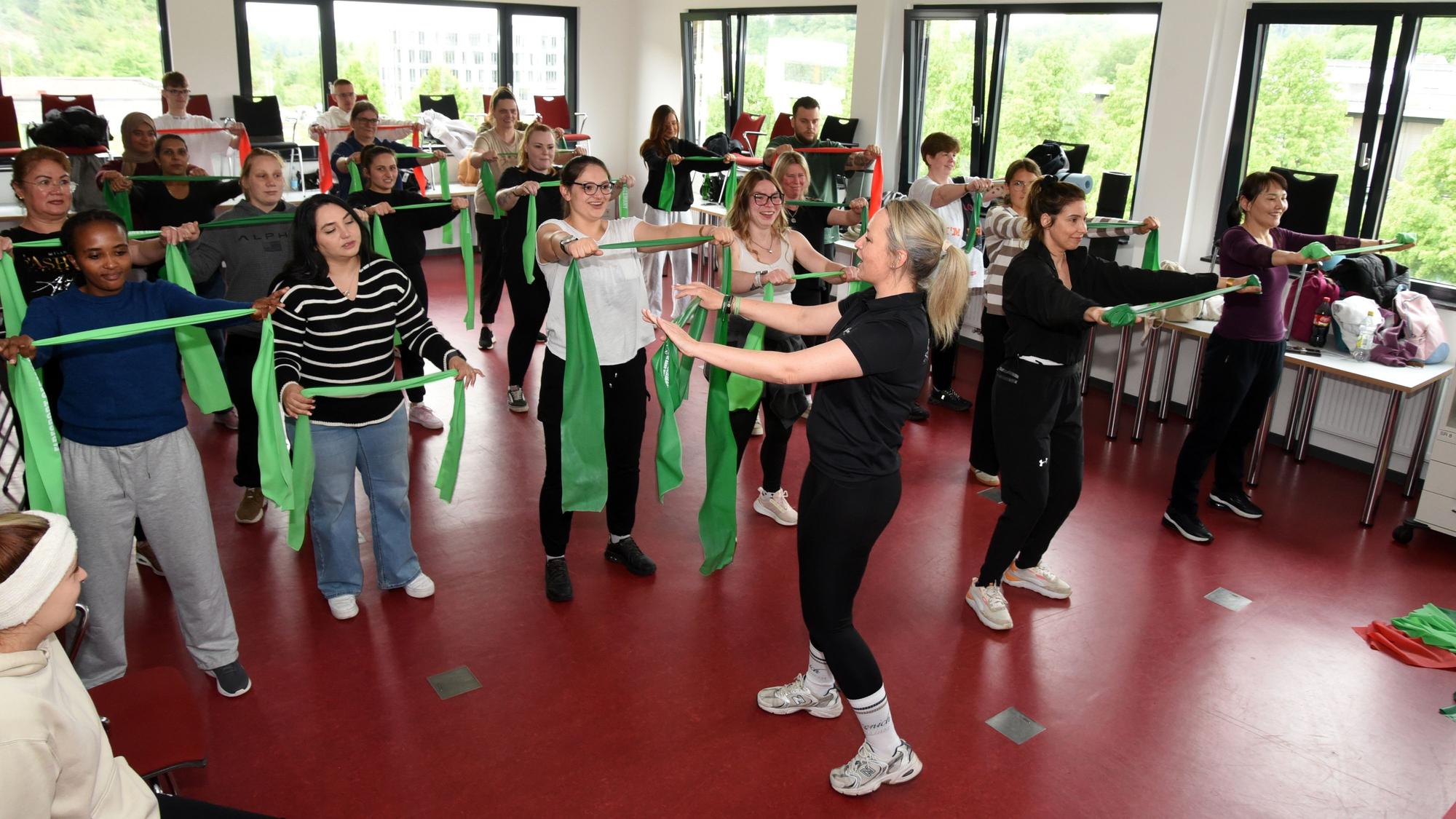 Eine Gruppe junger Menschen bei einer Fitnessübung mit grünen Fitnessbändern.
