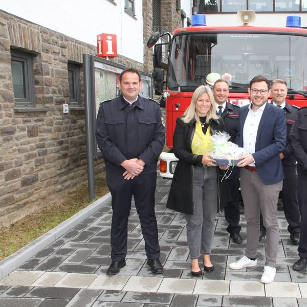 Die Obengenannten stehen vor einem Feuerwehrauto, Jennifer Meuren und Emmanuel Kunz halten ein Geschenk.