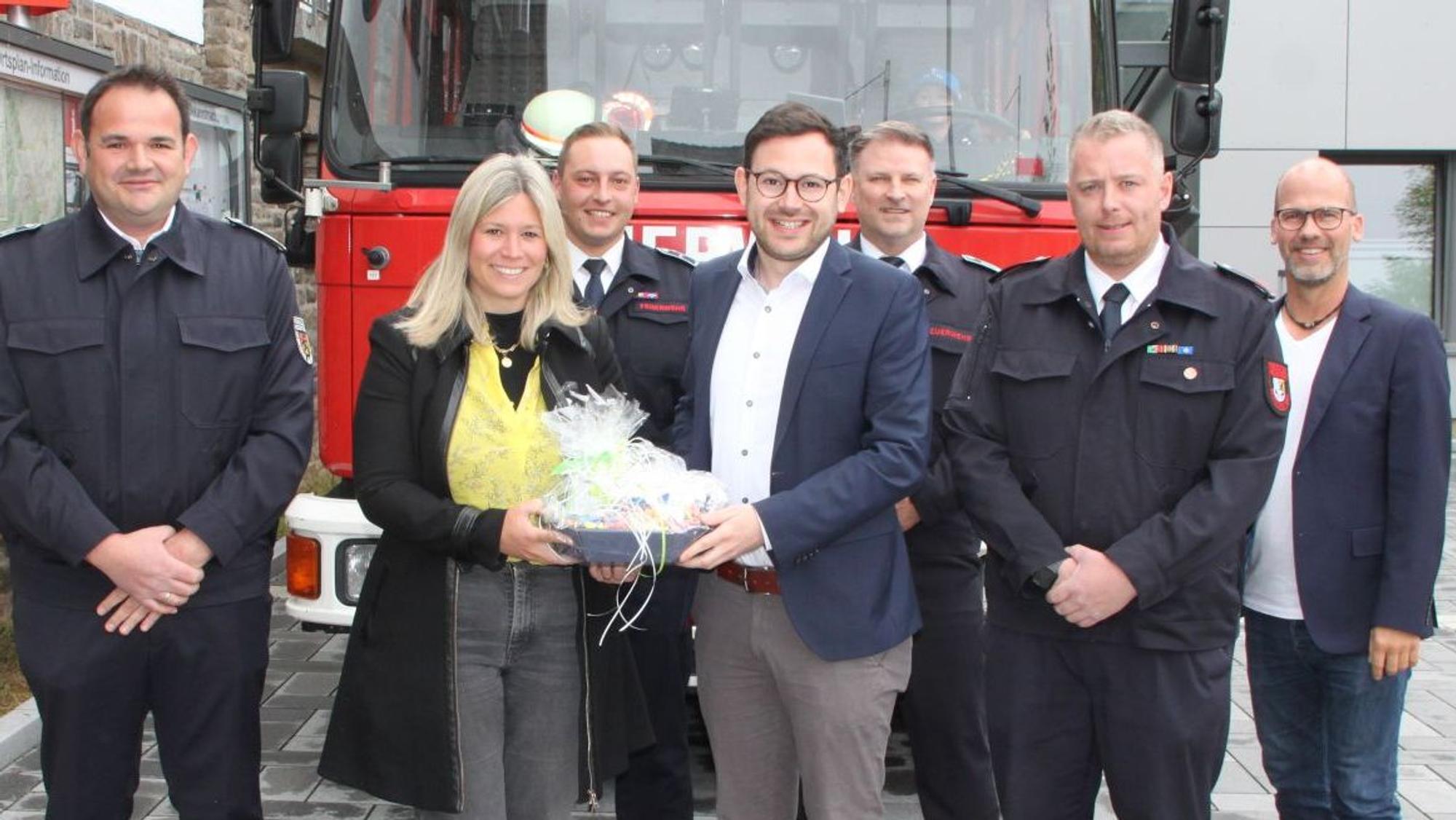 Die Obengenannten stehen vor einem Feuerwehrauto, Jennifer Meuren und Emmanuel Kunz halten ein Geschenk.