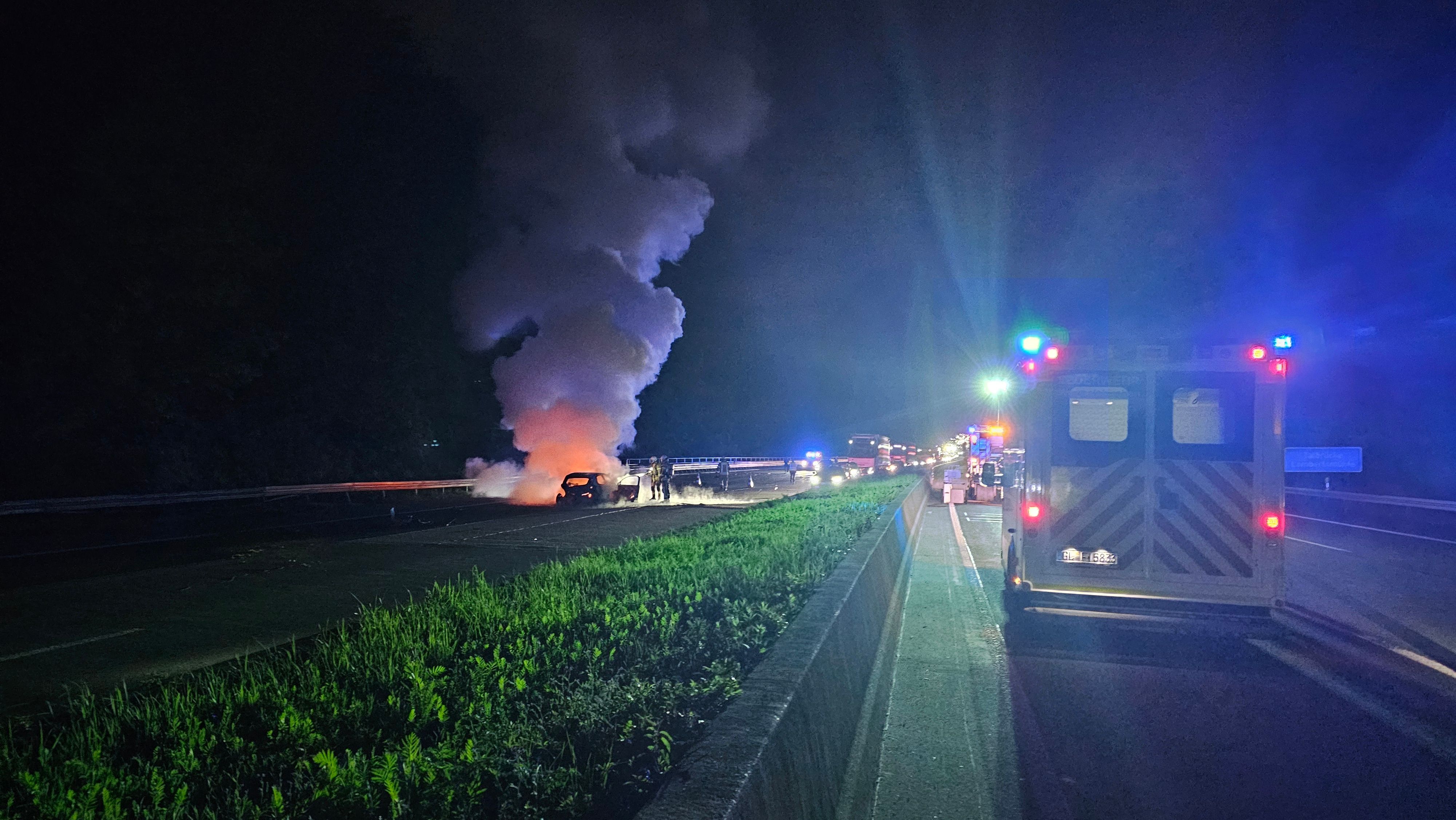 Feuerwehrleute löschen auf einer Autobahn ein in Flammen stehendes Auto.