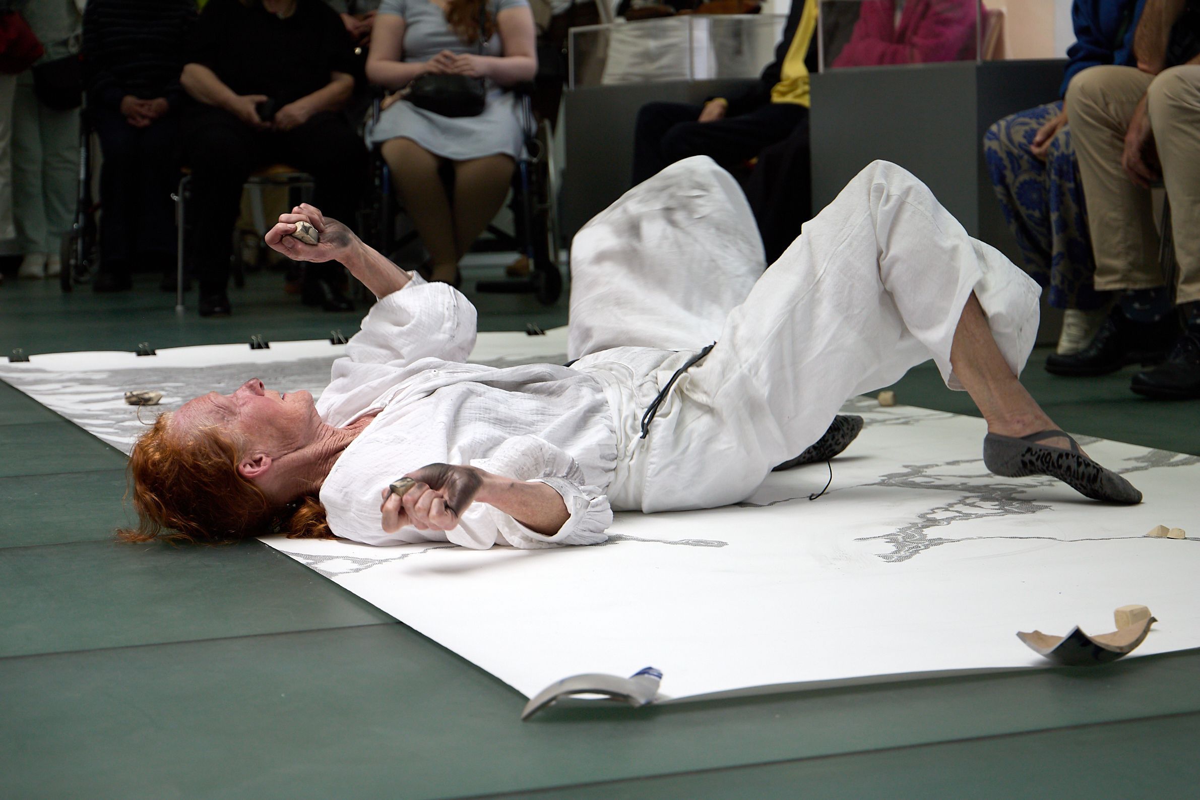 Die Künstlerin, die einen weißen Judo-Anzug trägt, liegt auf dem Rücken und rutscht über eine auf dem Boden ausgerollte Leinwand.
