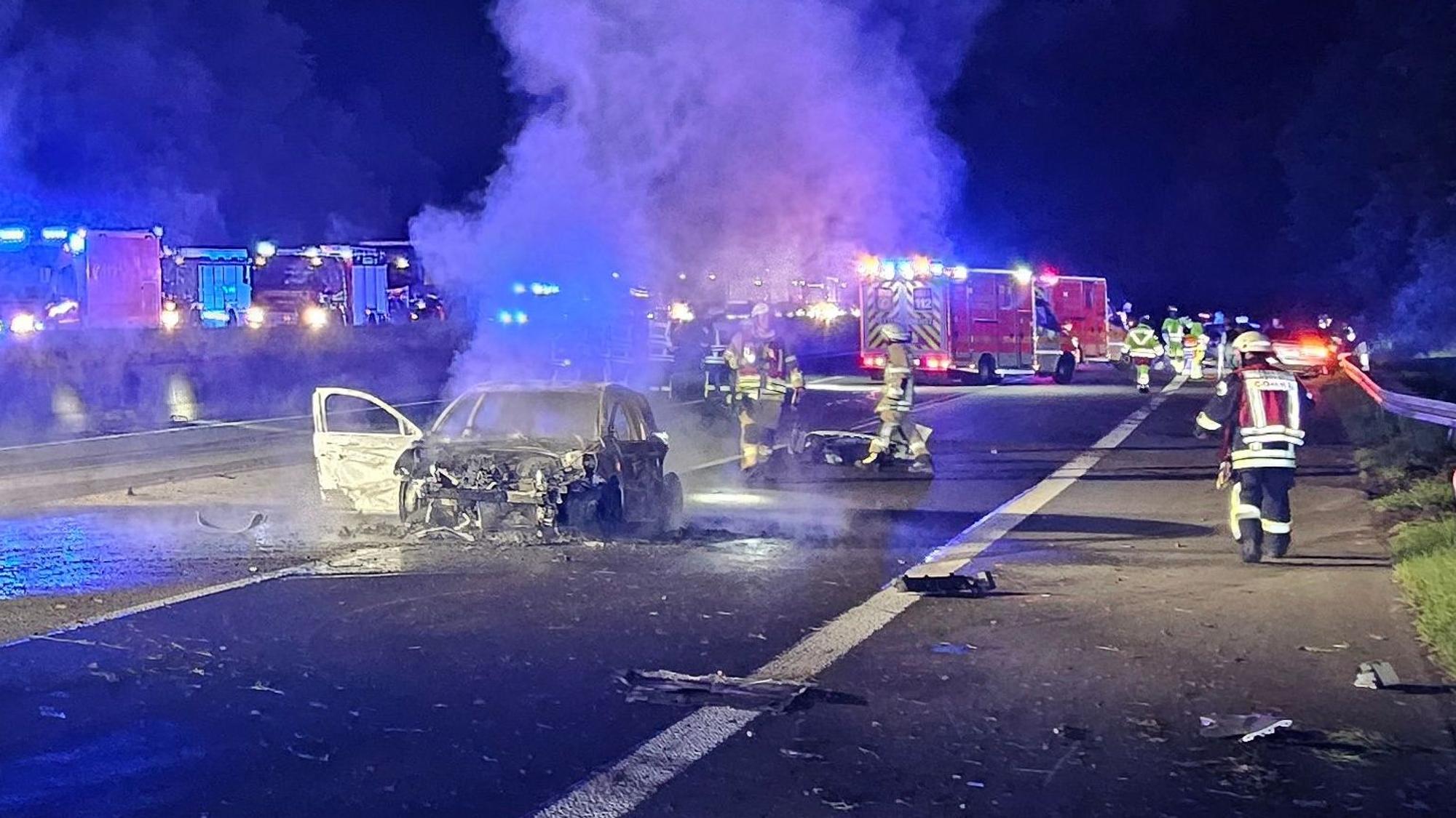 Feuerwehrautos stehen auf einer Autobahn in Höhe eines ausgebrannten Fahrzeugs.