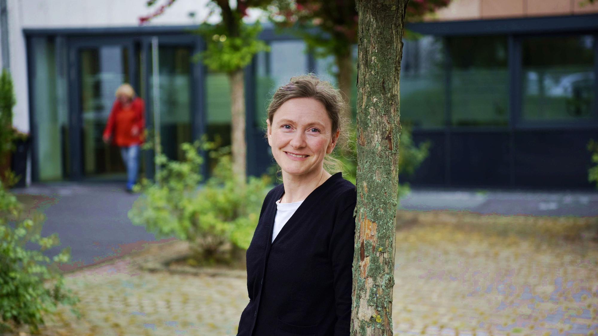Klimaschutzmanagerin Beatrix Brömme lehnt an einem Baum im Rathausinnenhof. Sie trägt einen schwarzen Pullover.