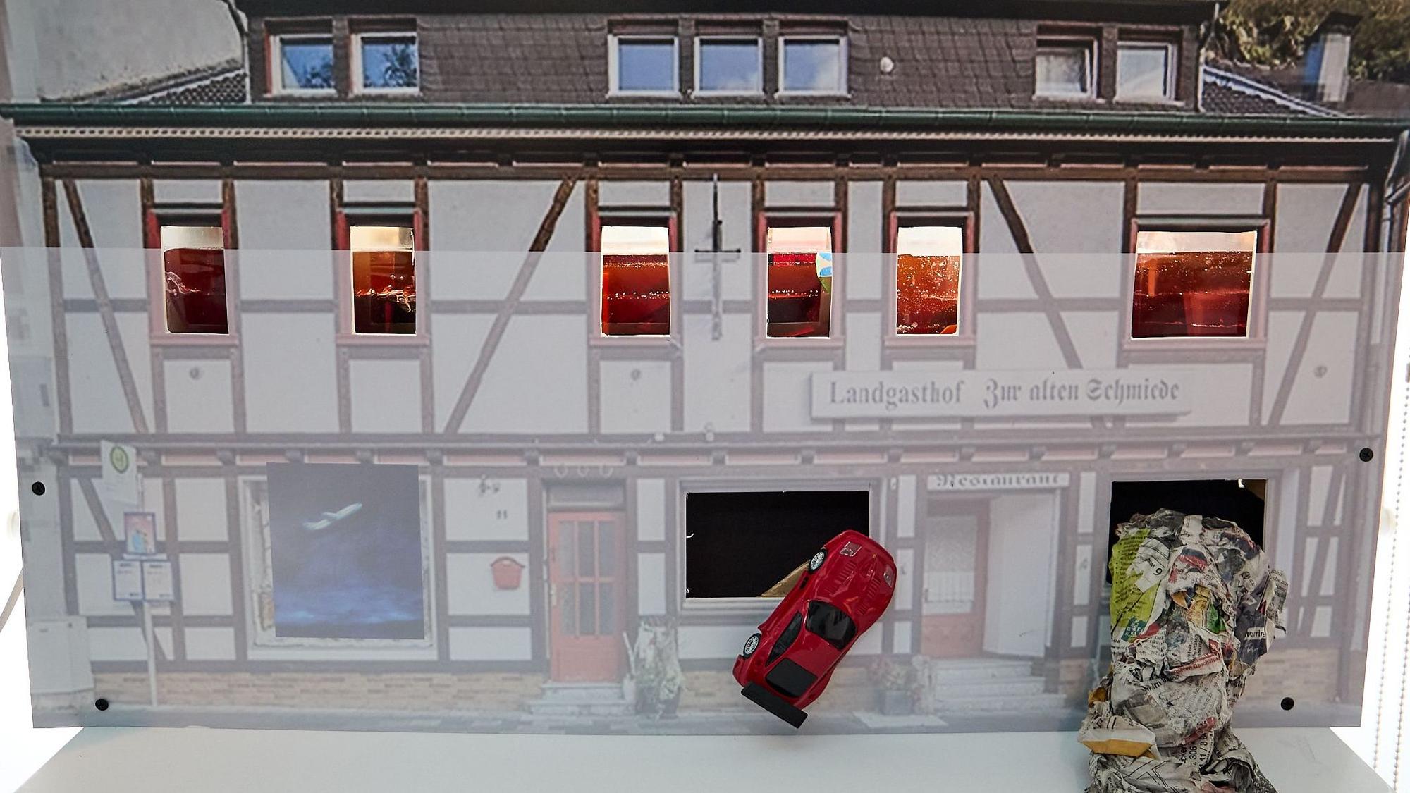 Eine matte Fläche zeigt, dass das Wasser im Fachwerkgebäude Des Landgasthofs Zur alten Schmiede bis zur Mitte des ersten Obergeschosses stand. Ein rotes Auto wurde gegen ein Fenster gespült. Aus einem anderen Fenster quillt Unrat.