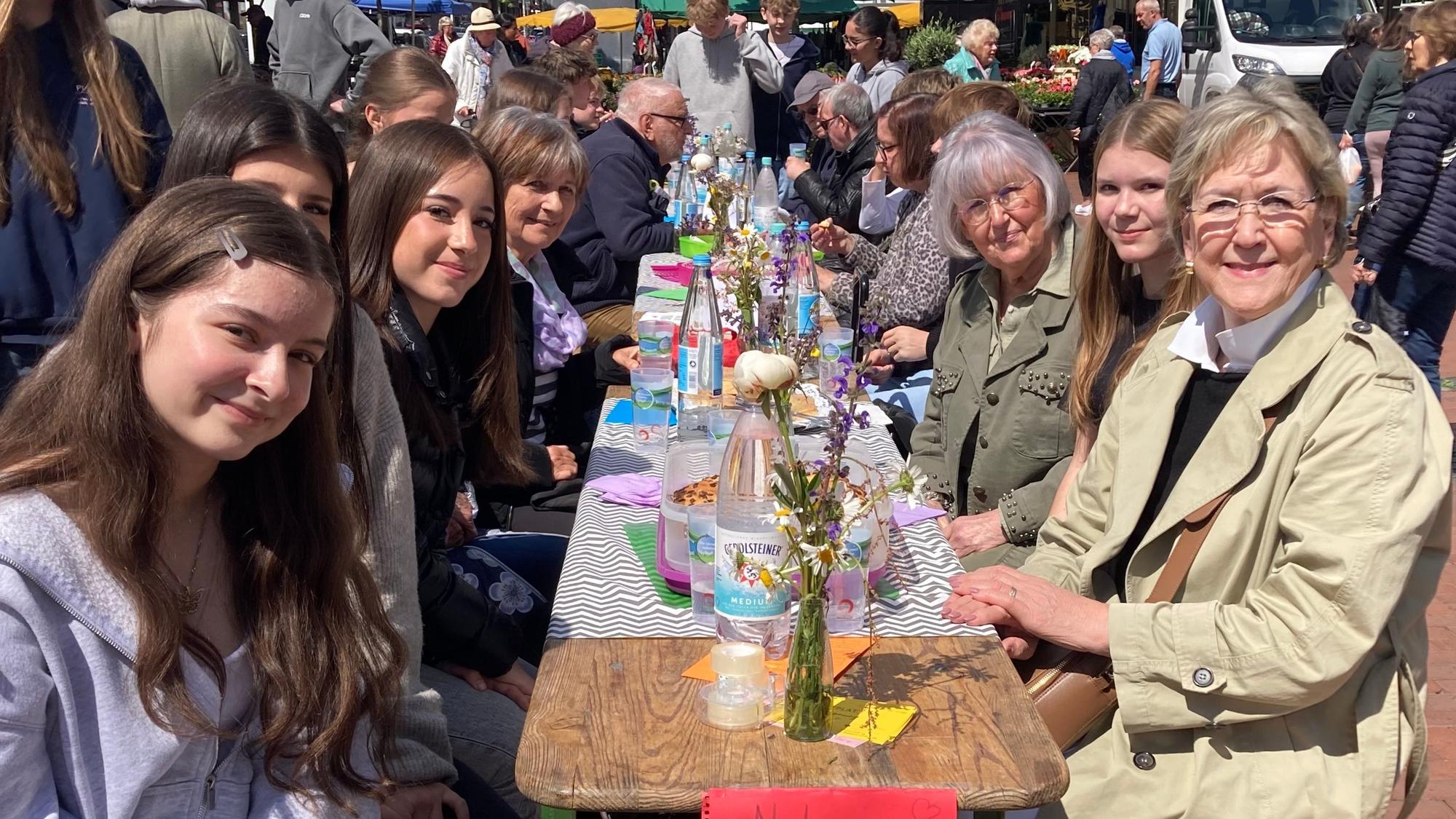Zu sehen sind Schülerinnen an einem Tisch mit Vertretern einer älteren Generation