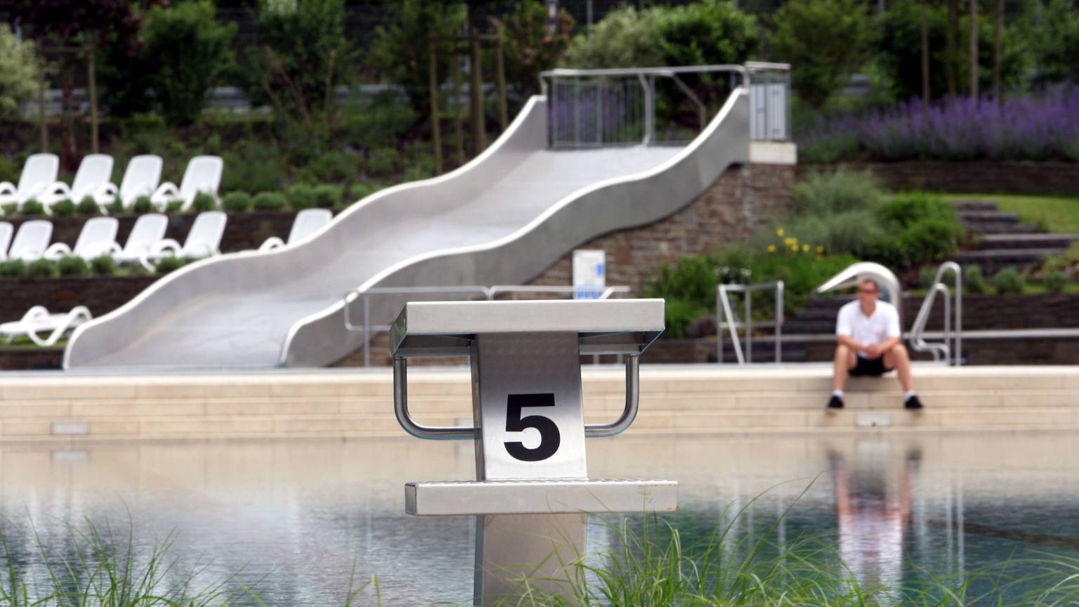 Ein Schwimmmeister sitzt am Rand des noch leeren Nichtschwimmerbeckens in Rösrath-Hoffnungsthal.