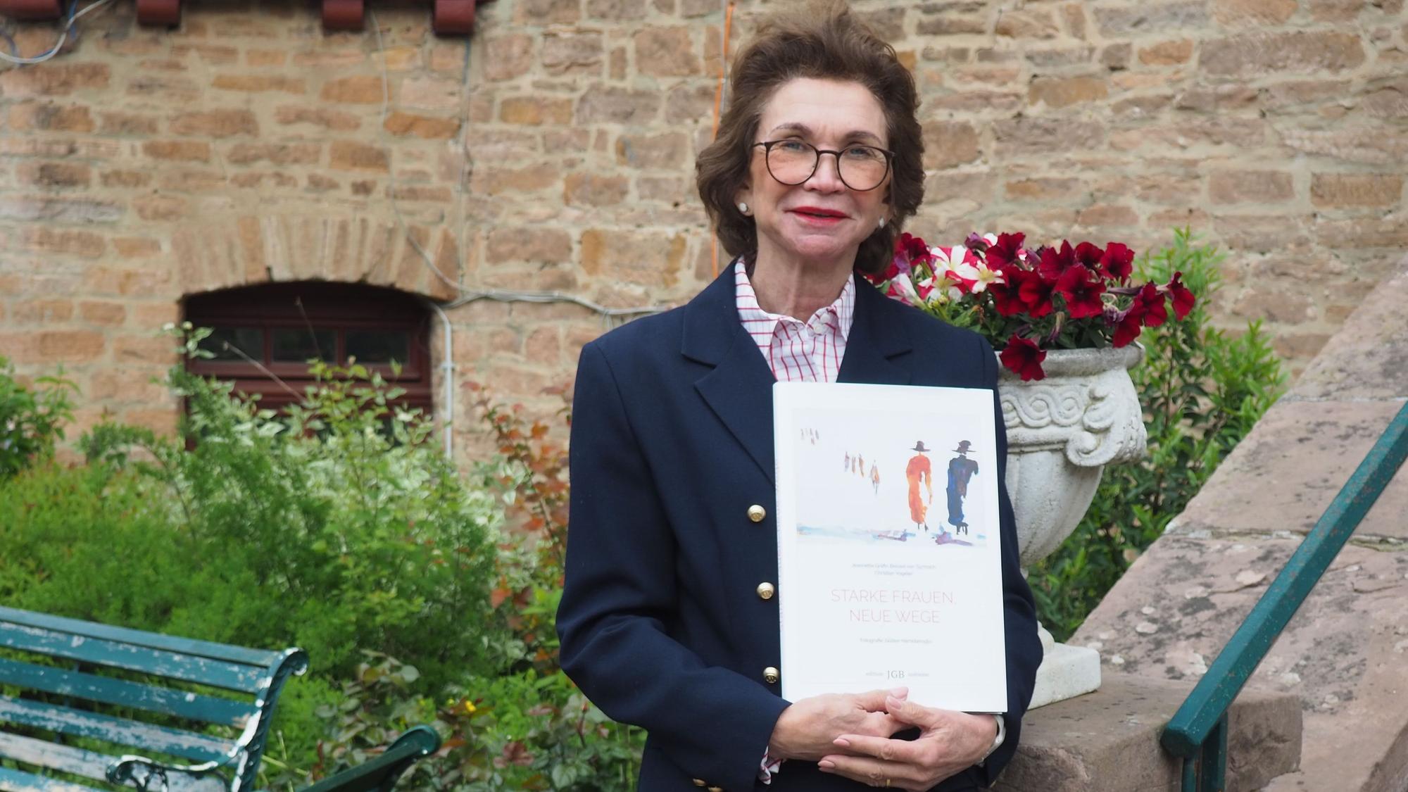 Jeannette Gräfin Beissel steht an der Treppe zur Burg und hält ihr Buch in den Händen.