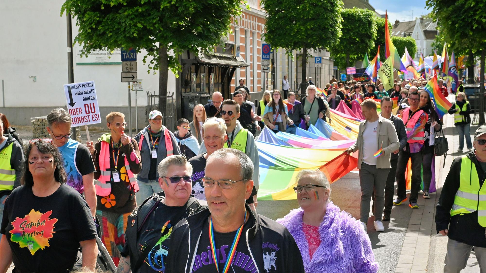Farbenfroh gekleidet zieht die lange Parade durch die Innenstadt. Mehrere Leute, darunter auch der Landrat und der Bürgermeister, tragen die große Pride-Flagge.