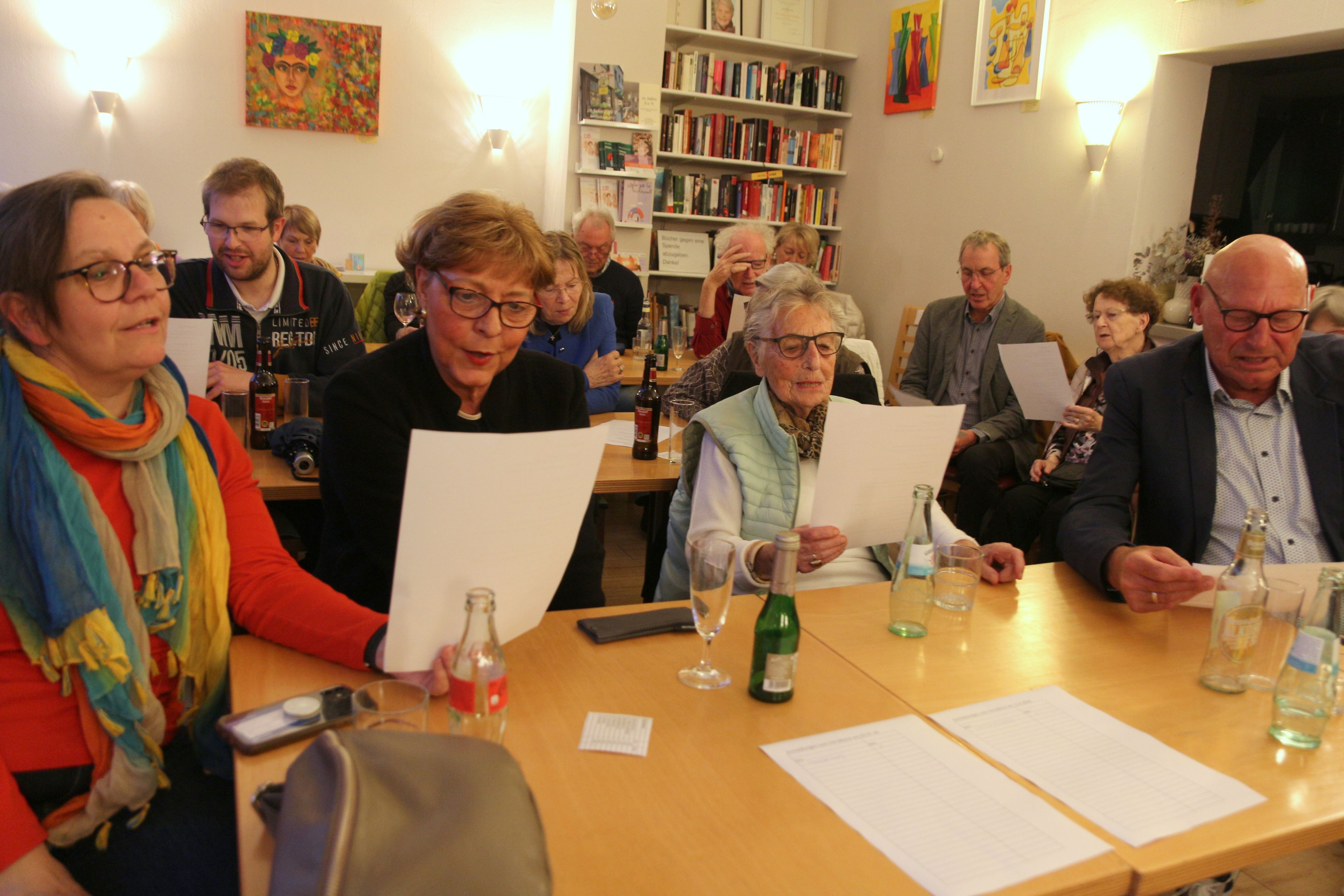Das Bild zeigt mehrere Gäste an Tischen, die Liedtexte in der Hand halten.