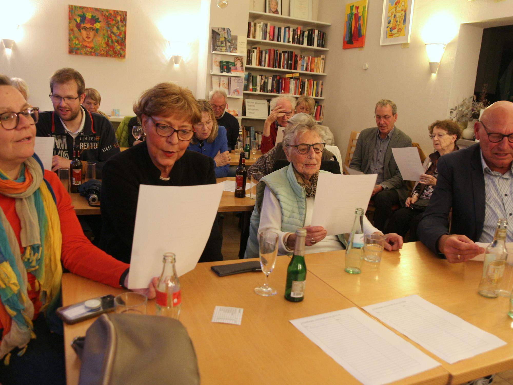 Das Bild zeigt mehrere Gäste an Tischen, die Liedtexte in der Hand halten.