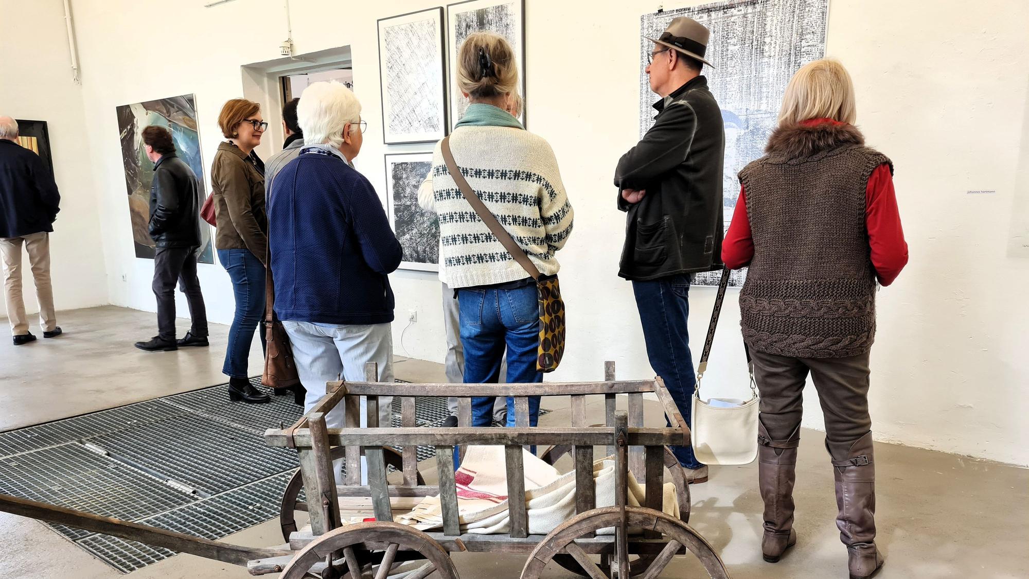Menschen stehen im Ausstellungsraum des Pumpwerks in Siegburg und betrachten Gemälde.
