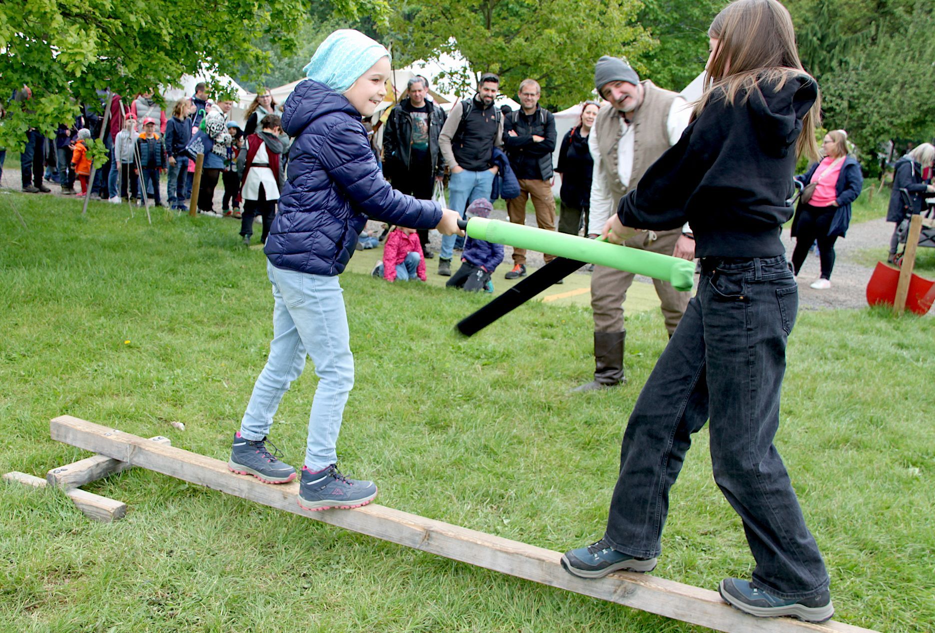 Die beiden Mädchen balancieren auf einem Balken und kämpfen mit Schaumstoff-Schwertern gegeneinander.