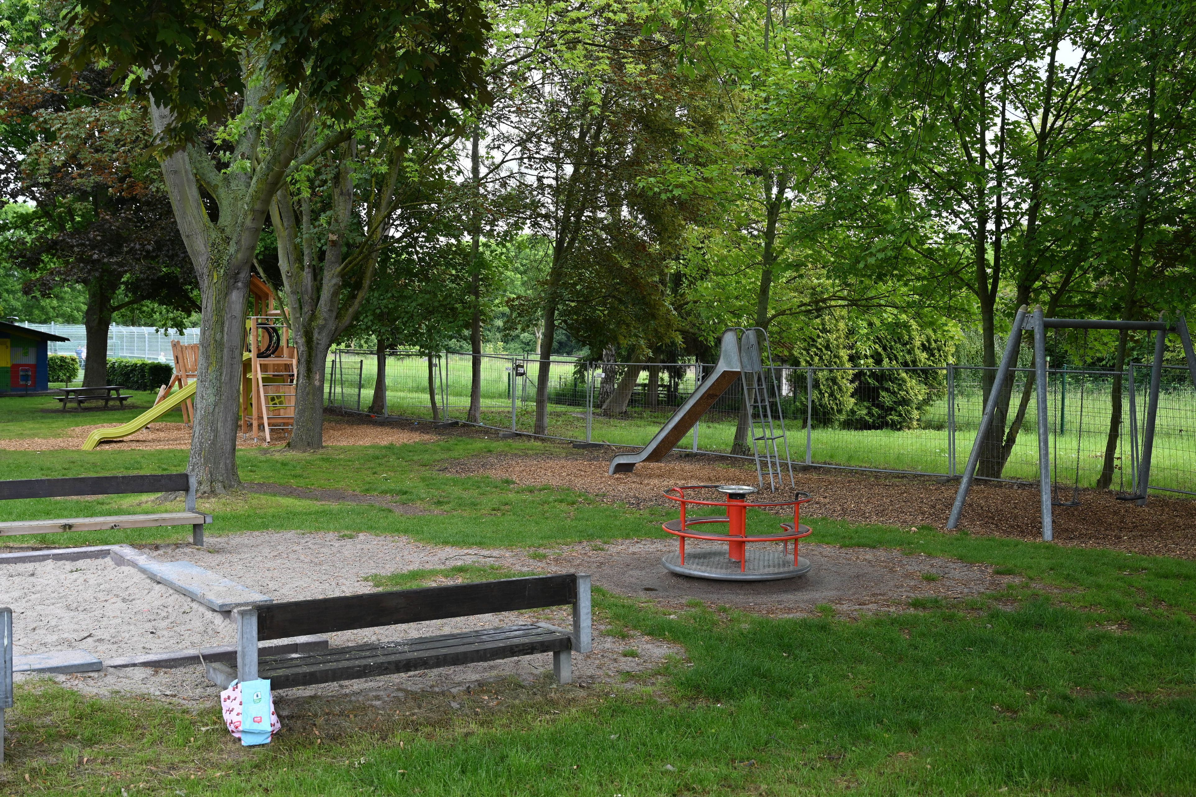 Das Bild zeigt den Spielplatz: Sandkasten, Bänke, Rutschen. Im Hintergrund ein Bauzaun, der auf die Erweiterung hinweist.
