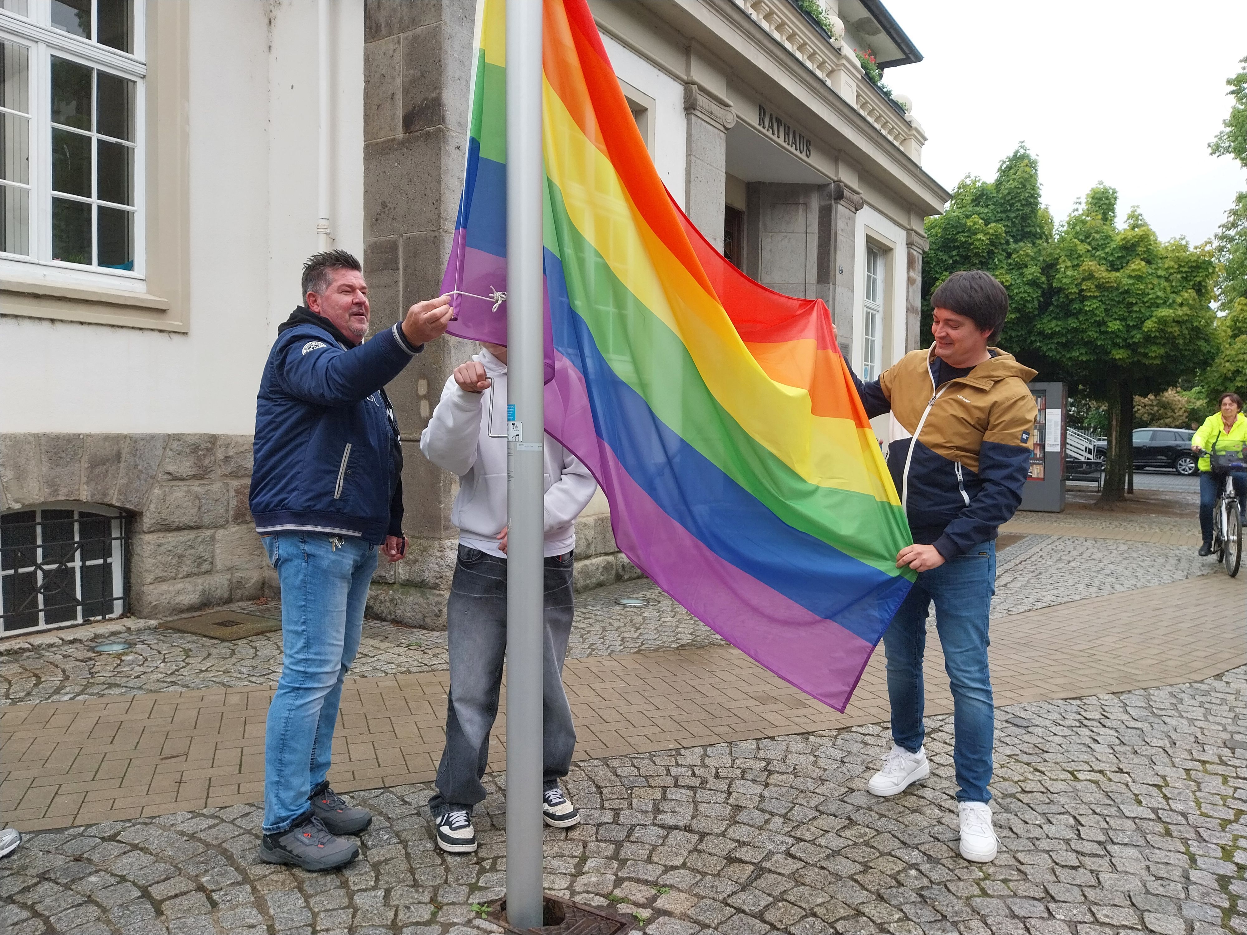 Drei Männer hissen eine Regenbogenfahne.