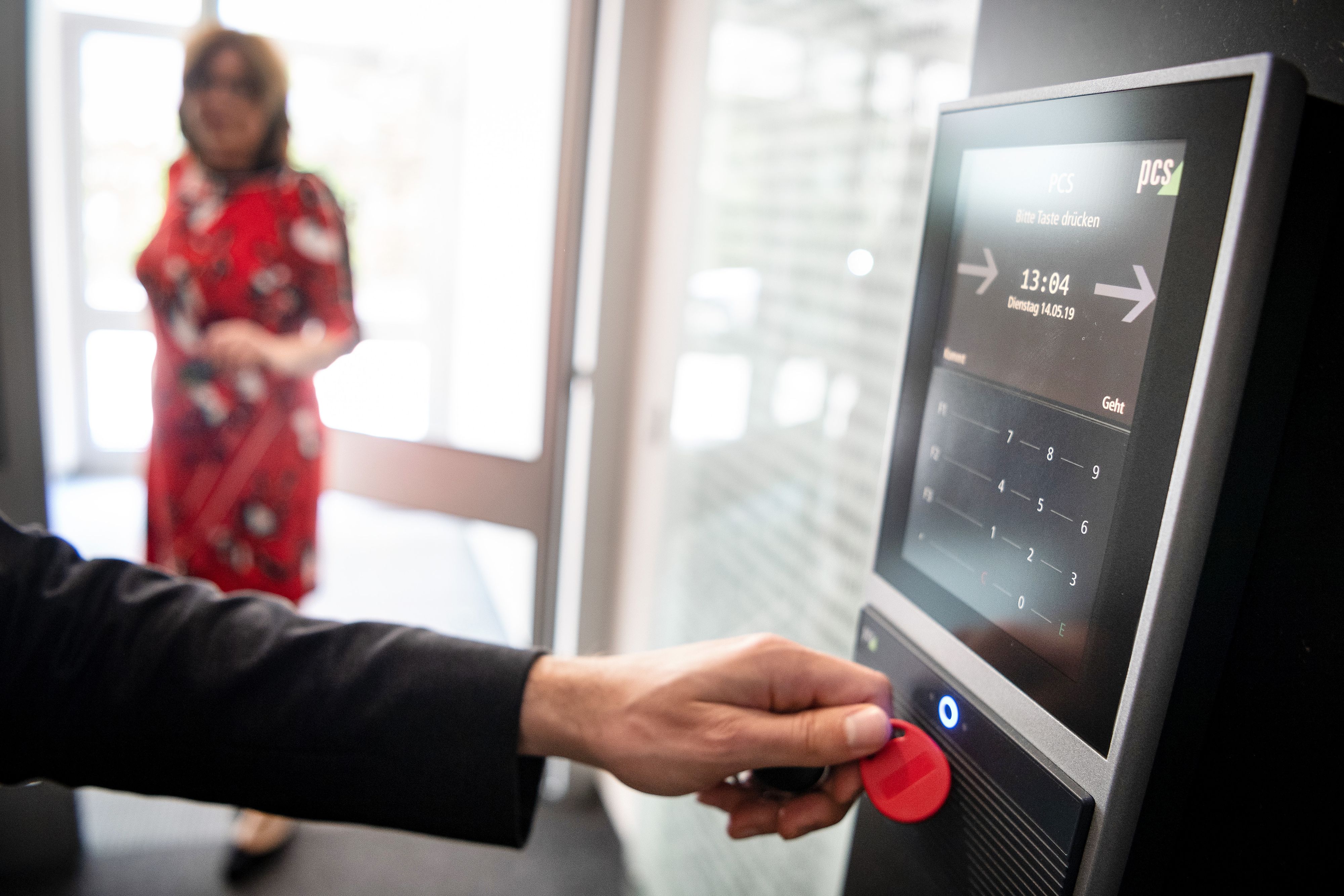 Eine Person hält einen roten Chip an ein Computer-Lesegerät um ihre Arbeitszeit zu erfassen.