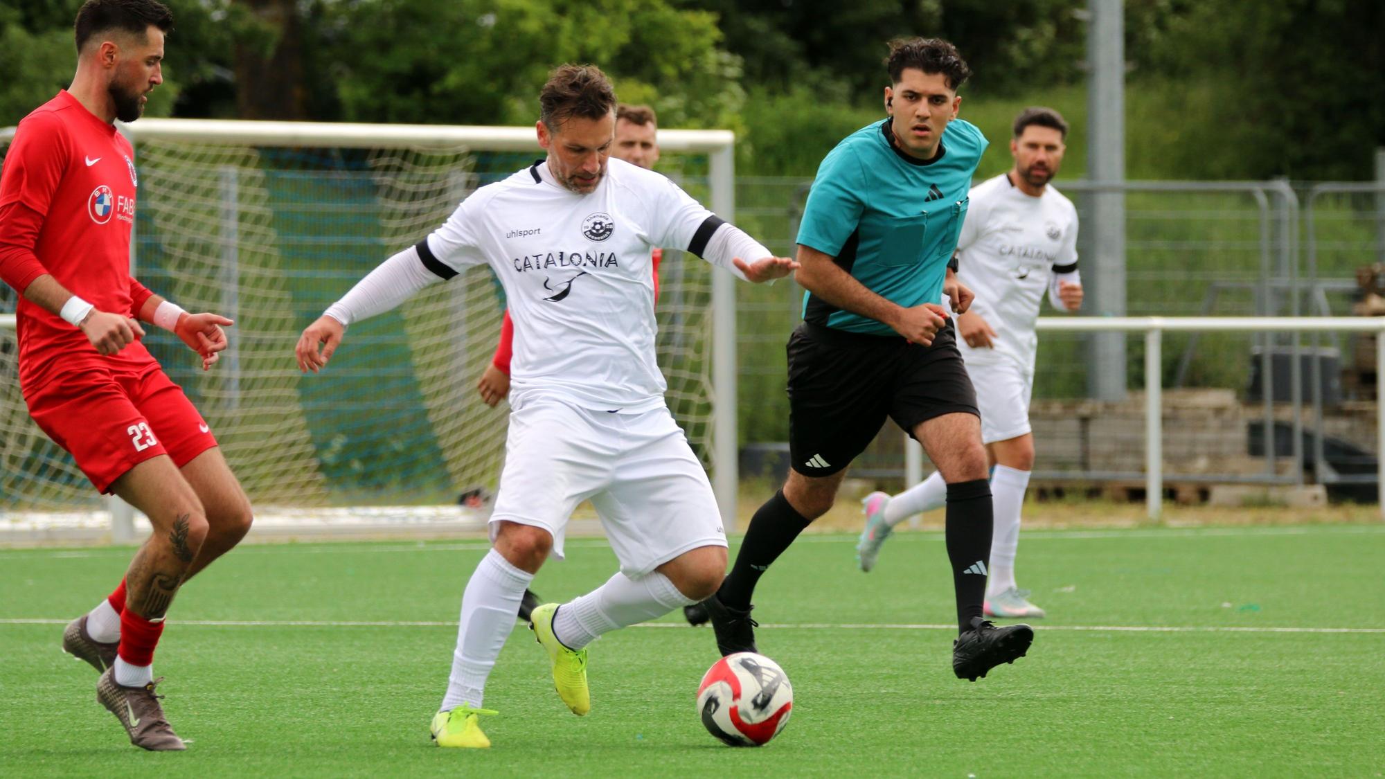 Athanasios Noutsos ist am Ball, ein Gegenspieler nähert sich ihm. Hinter ihm hat der Schiedsrichter alles im Blick.
