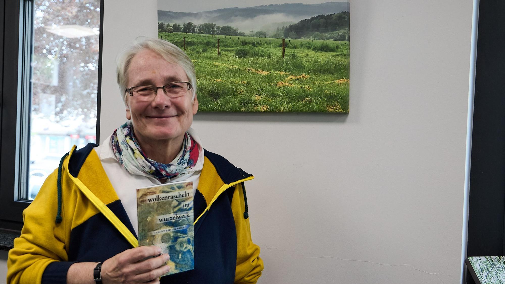 Eine Frau hält ein dünnes Buch in der Hand, das sie geschrieben hat.