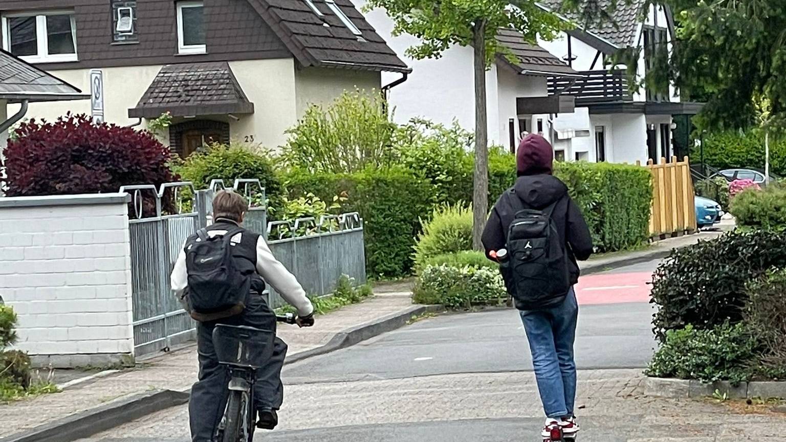 Ein Junge faährt auf dem Farrad, ein Junge auf dem Roller.